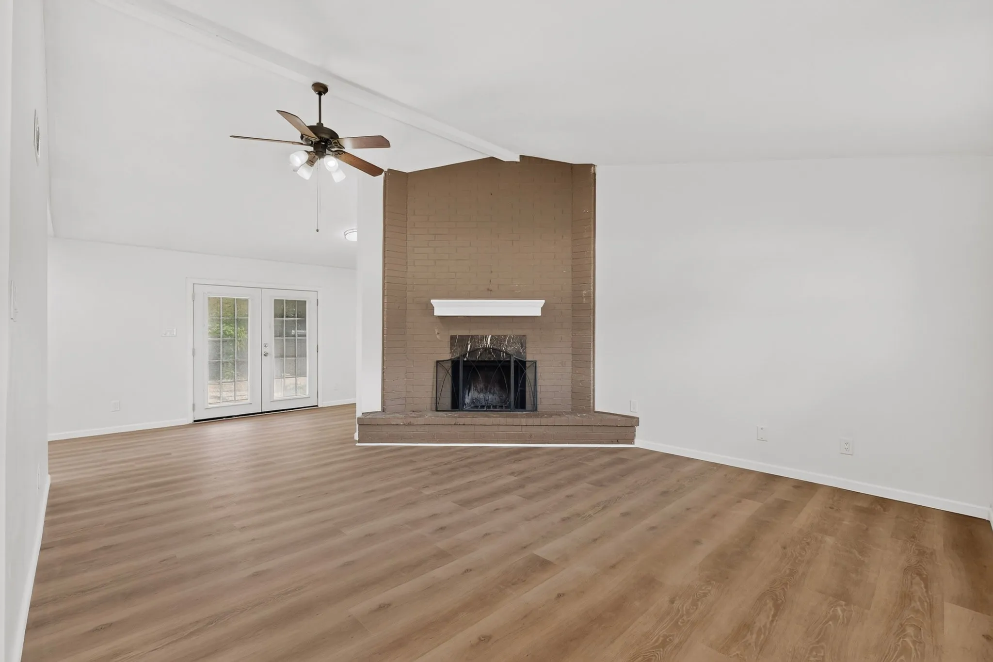 Vaulted ceiling with a ceiling fan, a brick fireplace with a white mantel, wood-finish flooring, and glass-paneled French doors