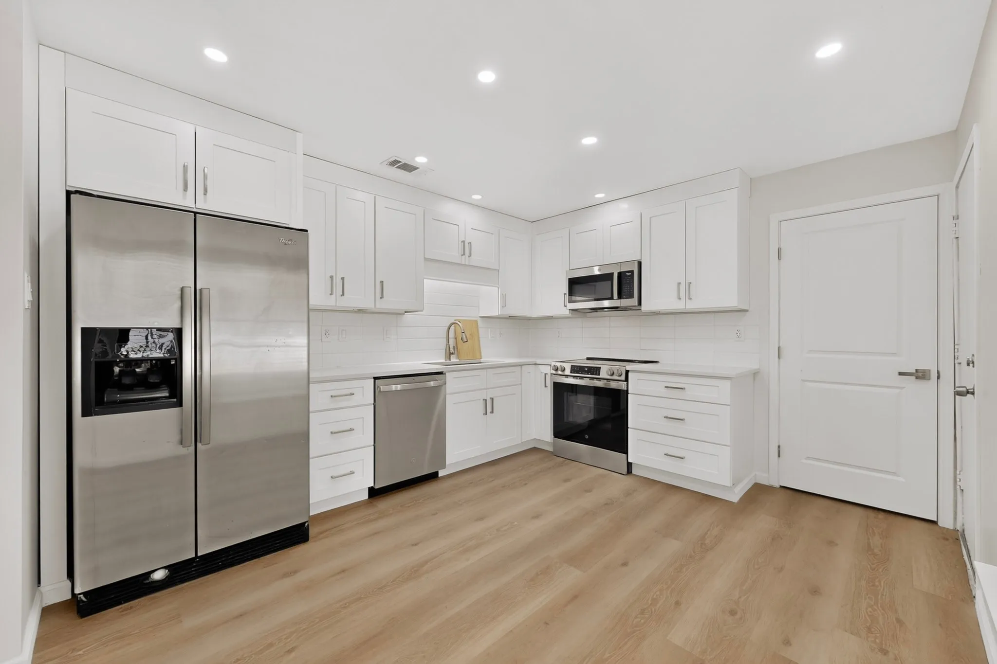 Kitchen featuring white shaker-style cabinetry, stainless steel appliances, a white tile backsplash, light-toned wood-finish flooring, and recessed lighting