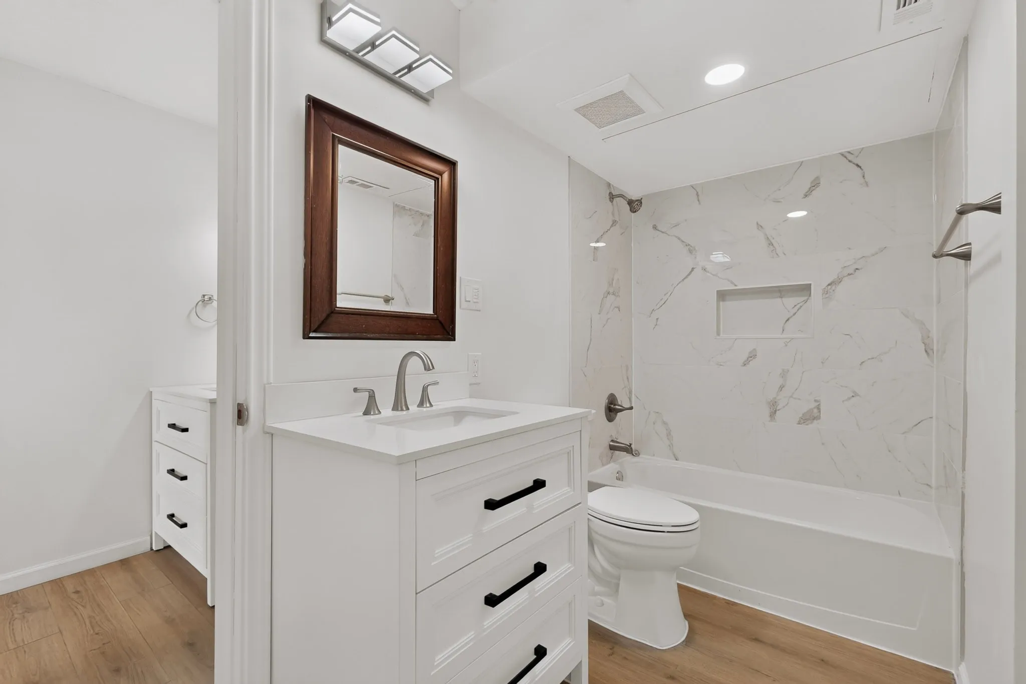 White vanity with a rectangular basin, brushed nickel faucet, and a framed mirror