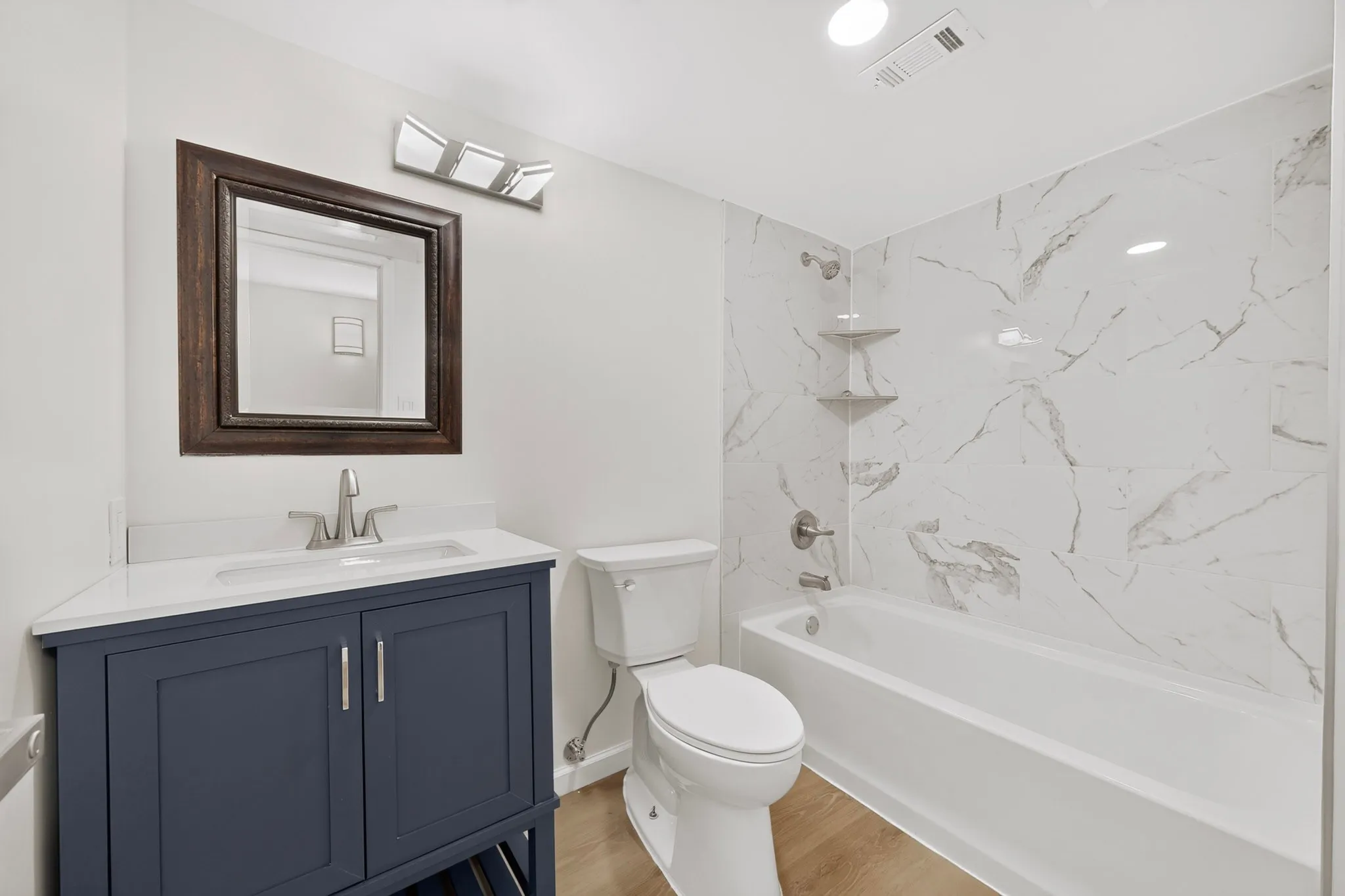 Bathroom featuring a navy blue vanity with white countertop, chrome fixtures, a framed mirror, and a tiled shower/tub combination with built-in shelving