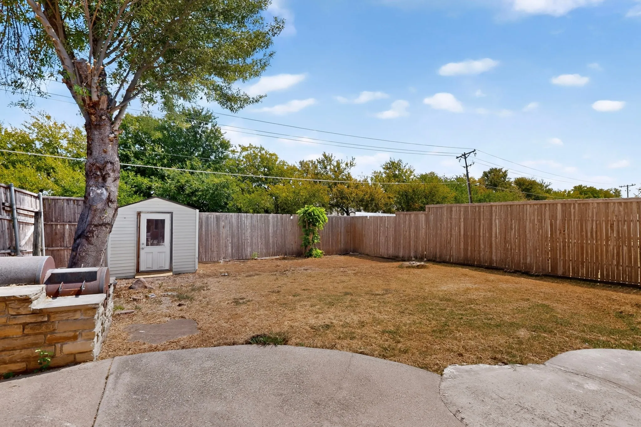 Expansive backyard with concrete patio, wood privacy fencing, mature tree, and storage shed