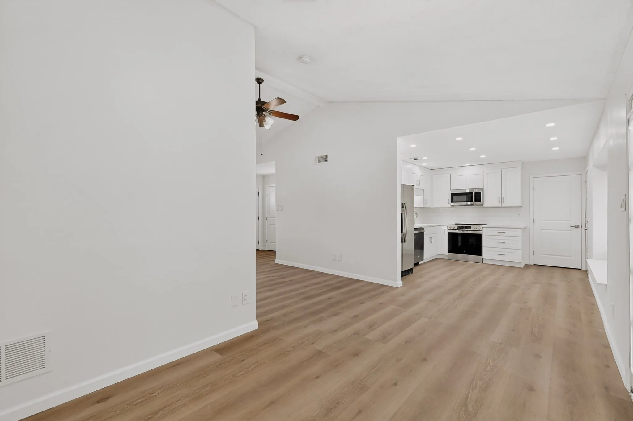Vaulted ceilings, wood-finish flooring, recessed lighting, ceiling fan, and a kitchen featuring white cabinetry and stainless steel appliances
