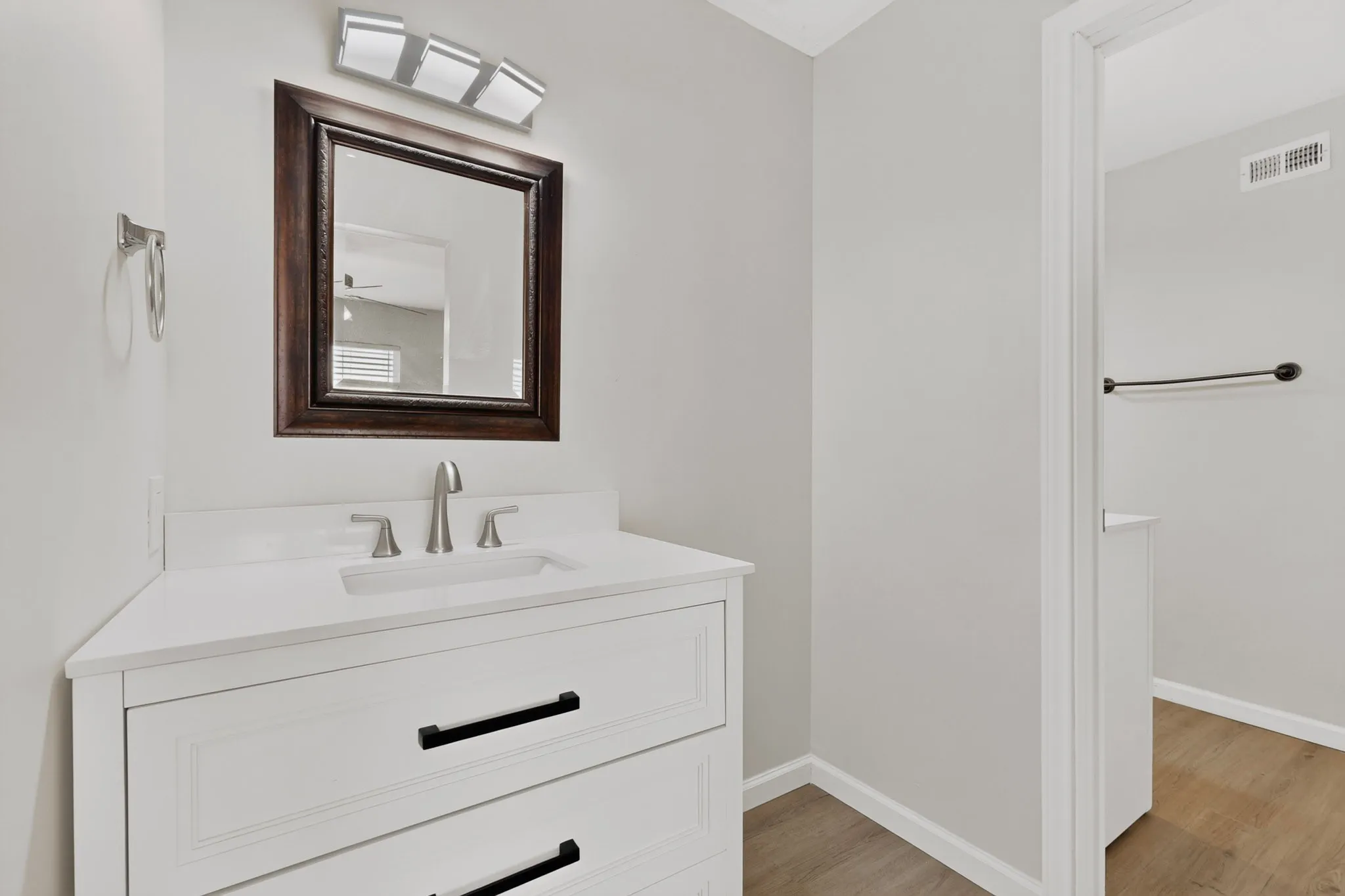 White vanity with an integrated sink, brushed nickel faucet, and dark-framed mirror