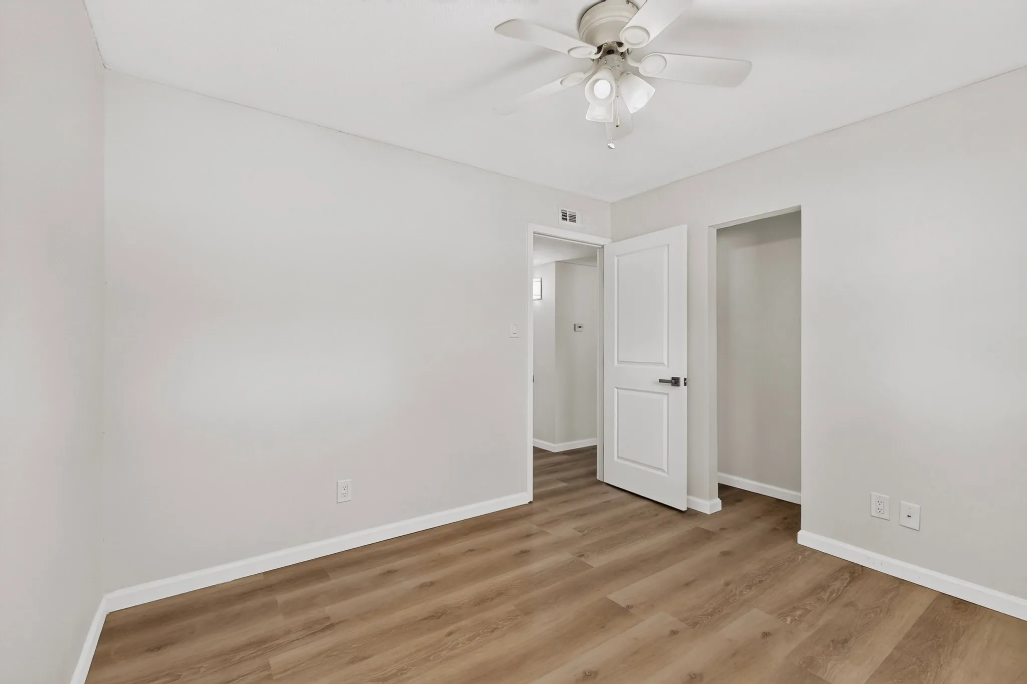 Neutral tone wall paint, wood-finish flooring, ceiling fan with light fixture, white interior door, and an open closet space