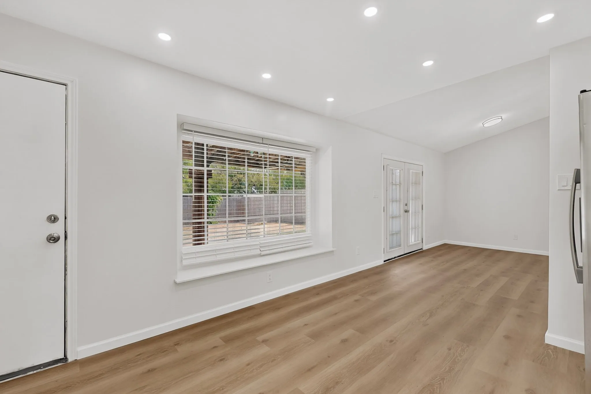 Recessed lighting, wood-finish flooring, white walls, large window with blinds, and French doors