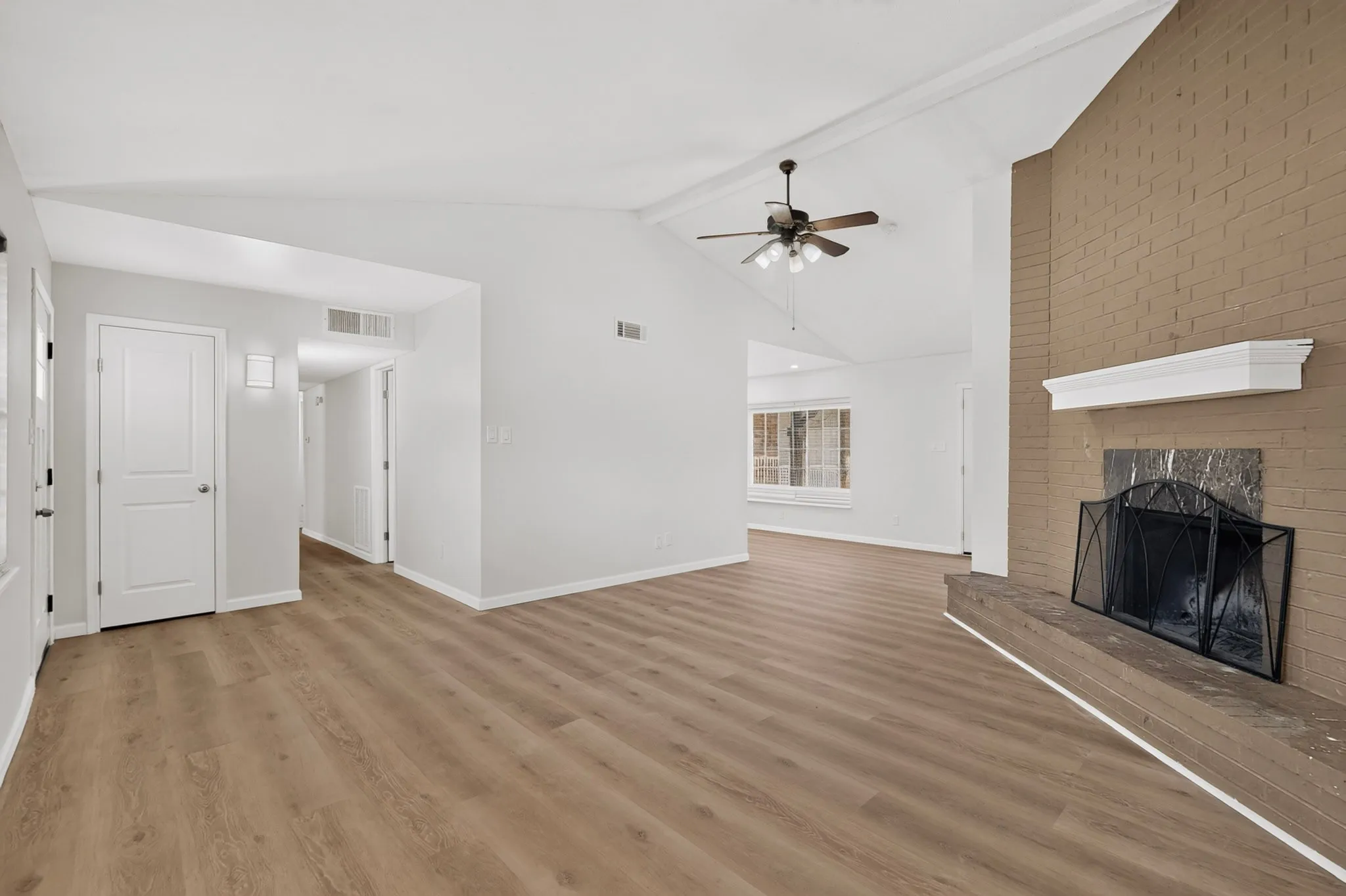 Vaulted ceiling with a ceiling fan, wood-finish flooring, brick-faced fireplace with a mantel, and white interior doors