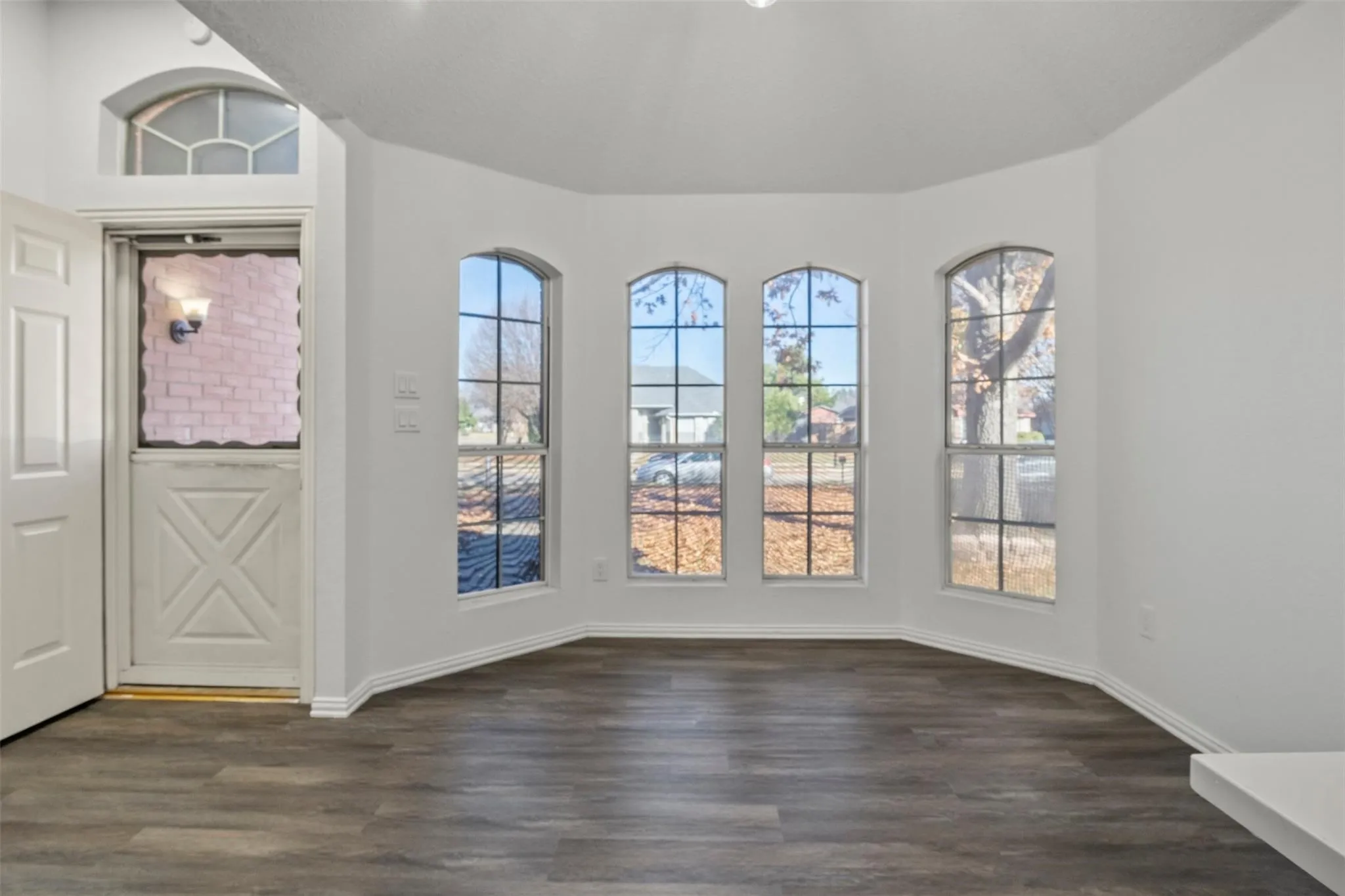 Bay window with three arched windows, wood-finish flooring, white walls, and a Dutch-style entry door with an arched transom