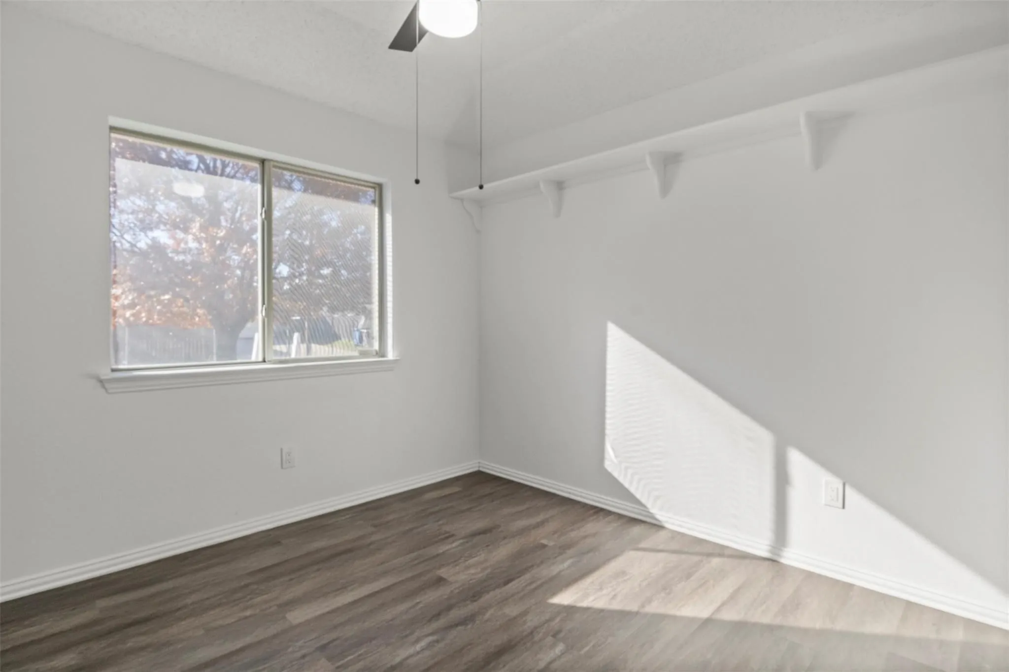 Wood-finish flooring, white walls, and a ceiling fan with integrated lighting
