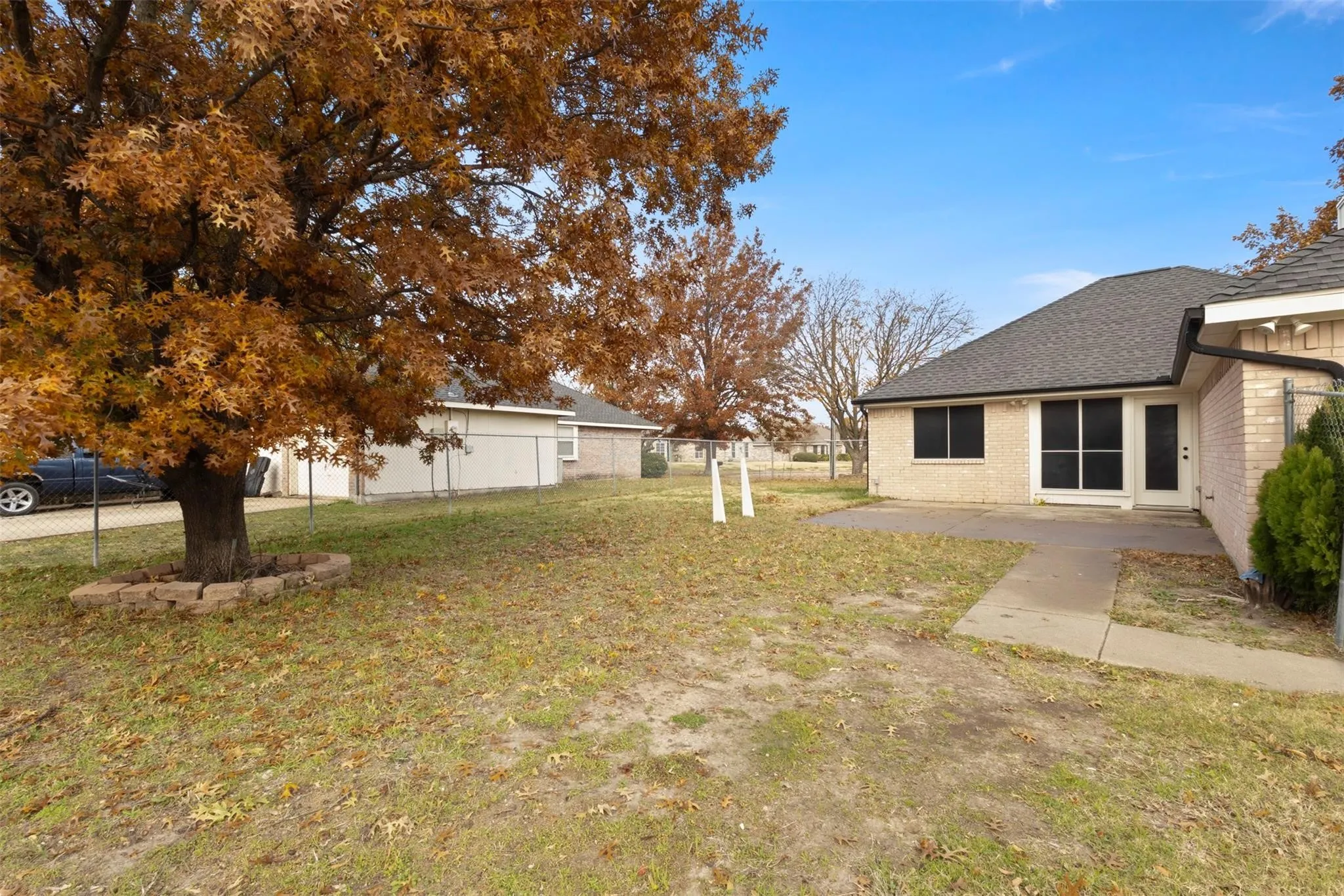 Brick exterior home featuring a concrete patio and a mature tree with a stone-edged tree ring