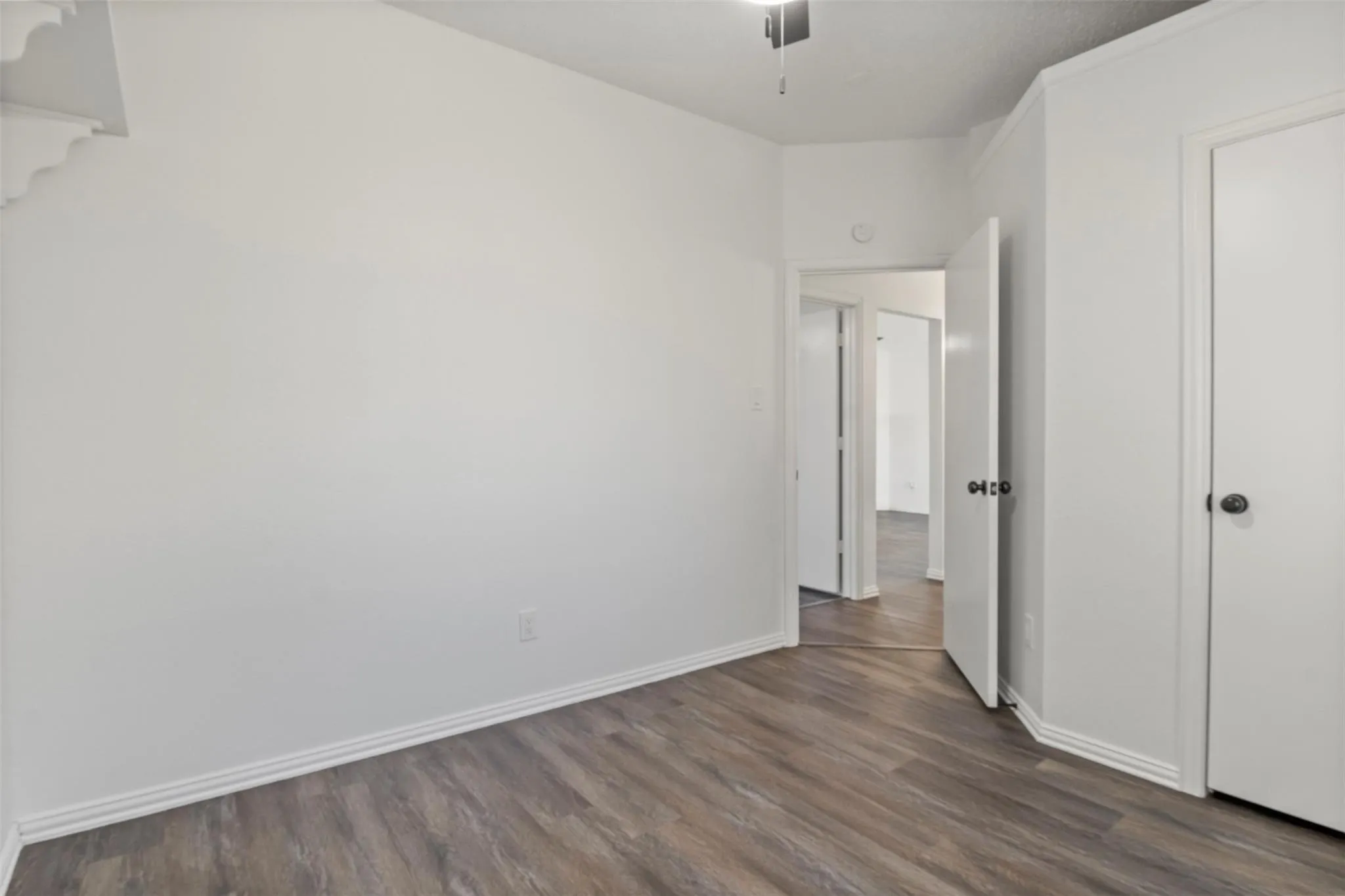 Wood-finish flooring with white baseboards, white paneled doors with dark hardware, and a ceiling-mounted fan