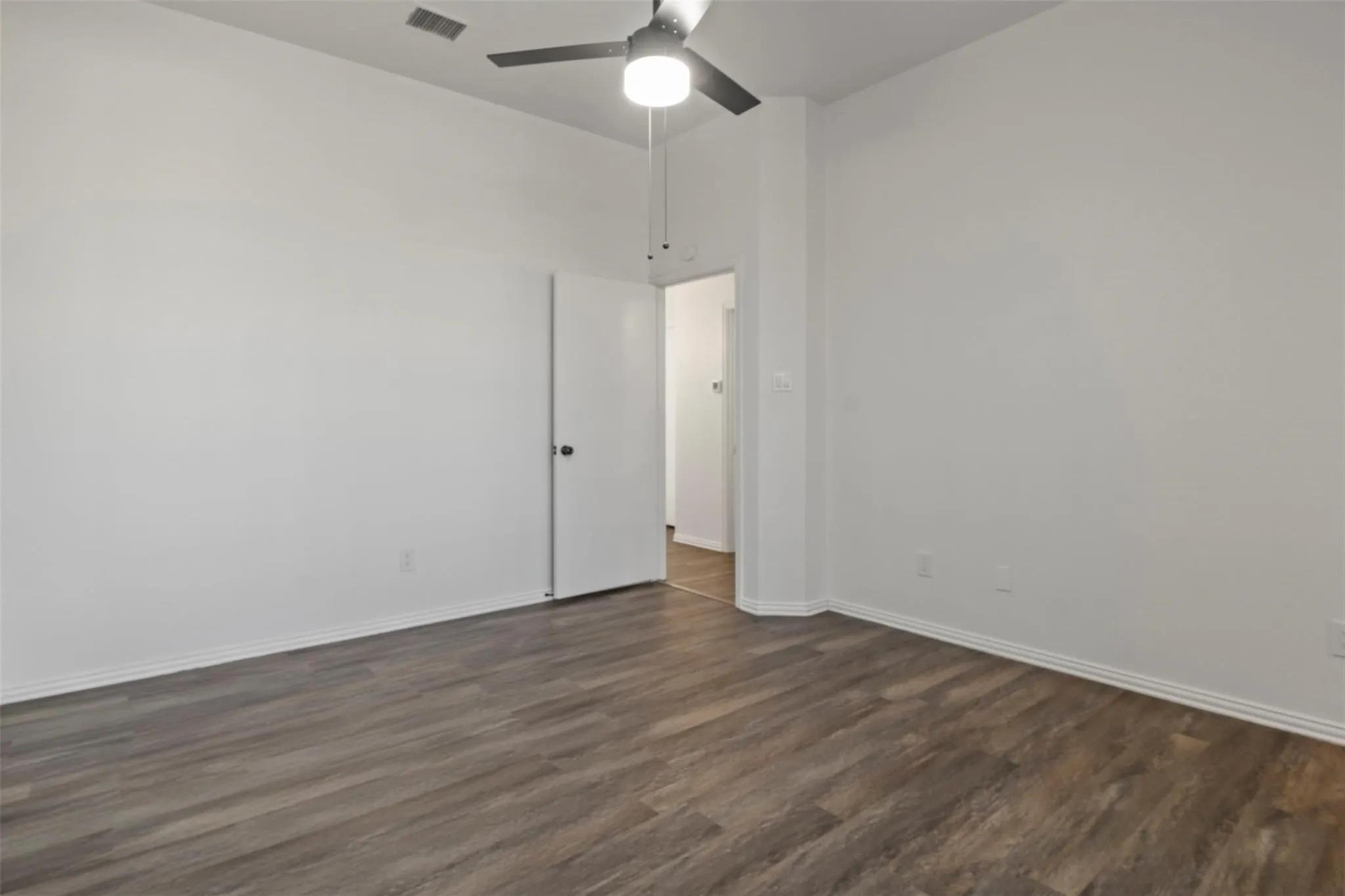 Wood-finish flooring with white baseboards, a ceiling fan with integrated lighting, and a white interior door