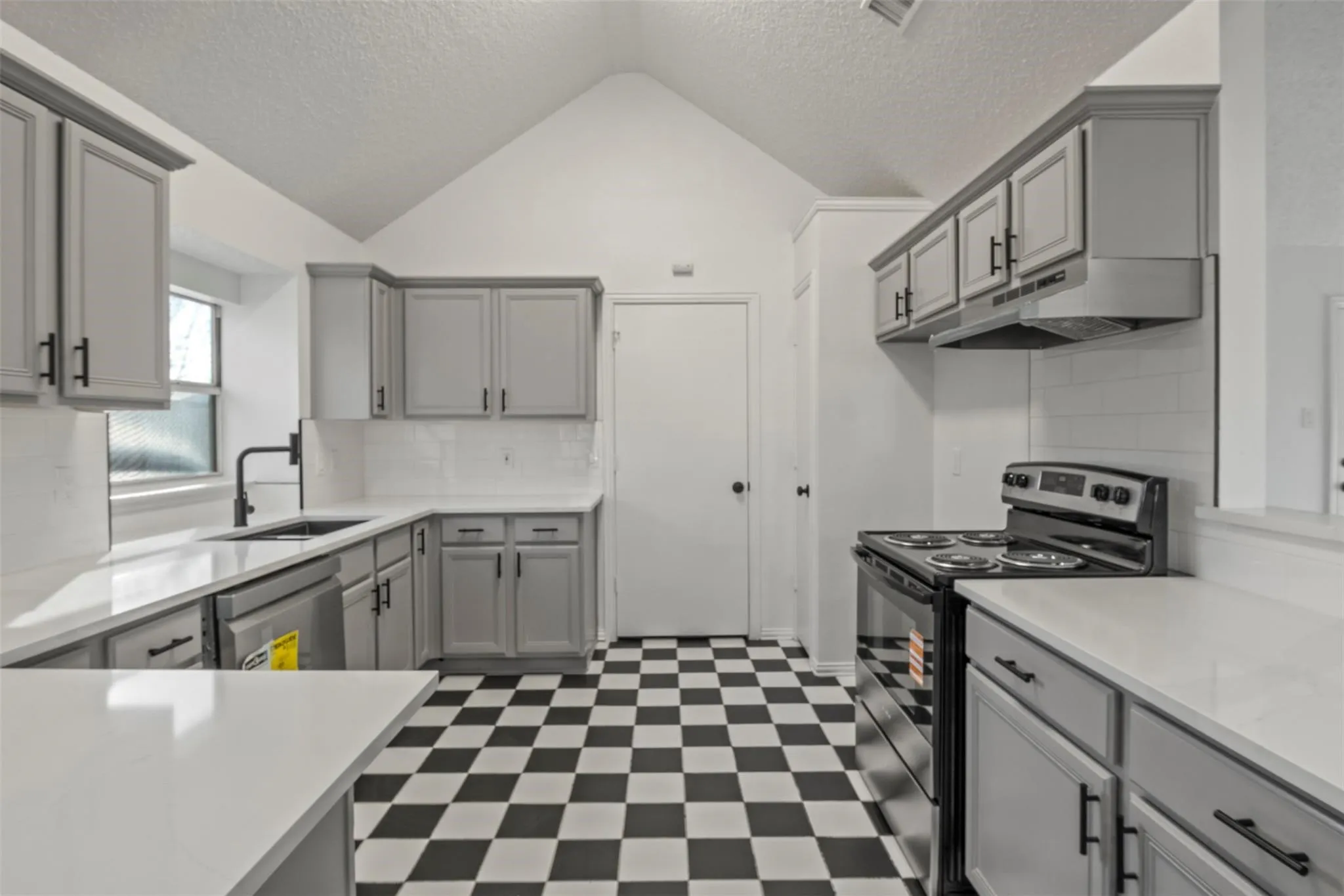 Kitchen featuring a vaulted ceiling, checkerboard flooring, white subway tile backsplash, light gray cabinetry, and white countertops
