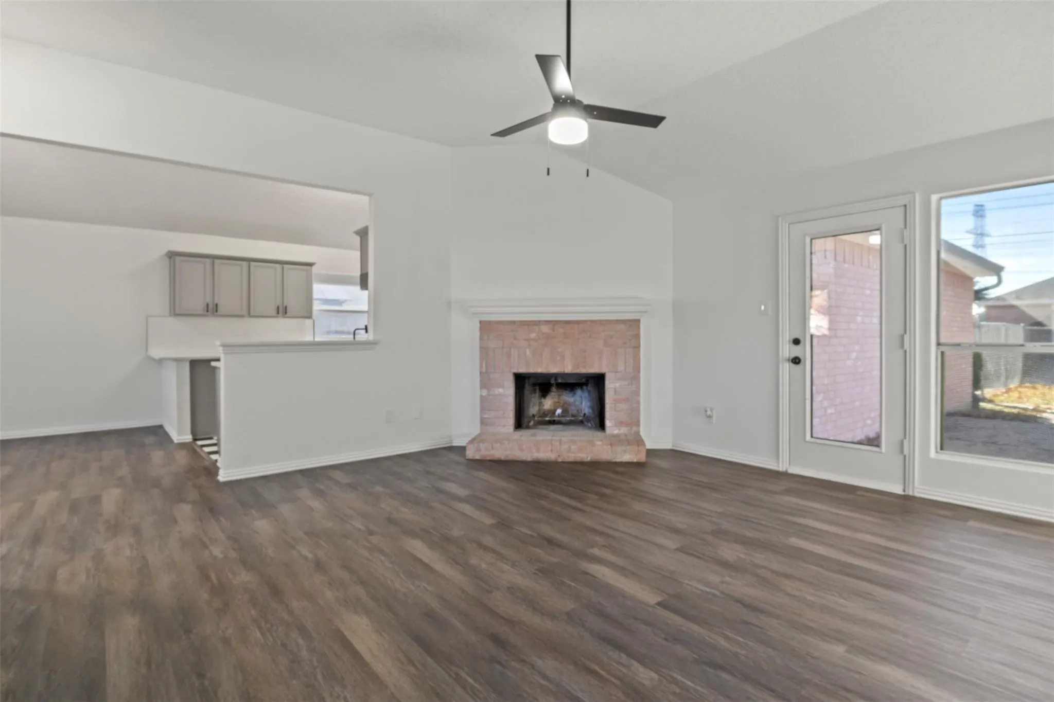 Vaulted ceilings, wood-finish flooring, brick fireplace, ceiling fan, and backyard access door