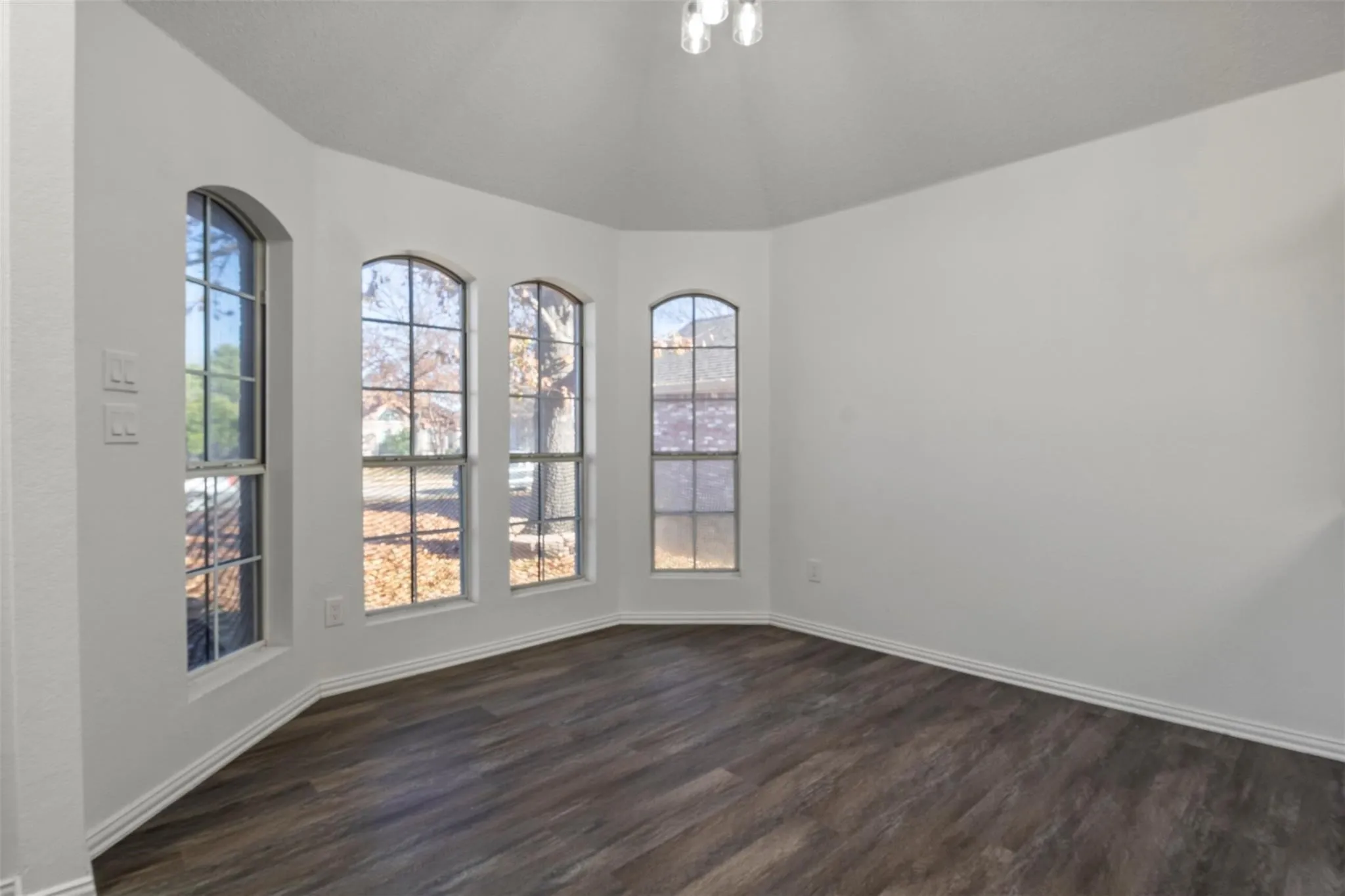 Bay window with arched top windows, wood-finish flooring, white baseboards, and a semi-flush mount ceiling light fixture