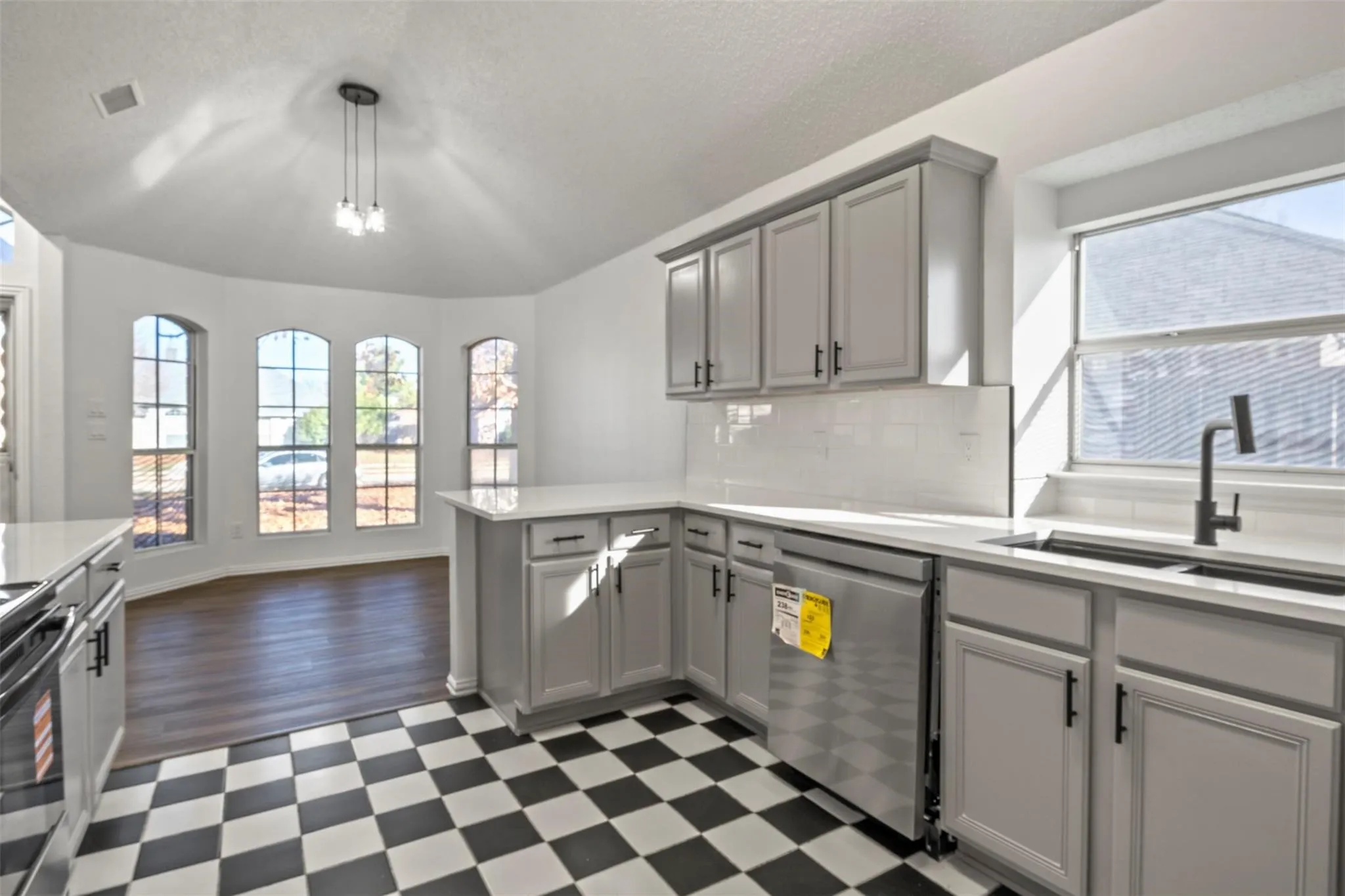 Kitchen featuring checkerboard flooring, light gray cabinetry with black hardware, stainless steel dishwasher, white countertops, and a white subway tile backsplash