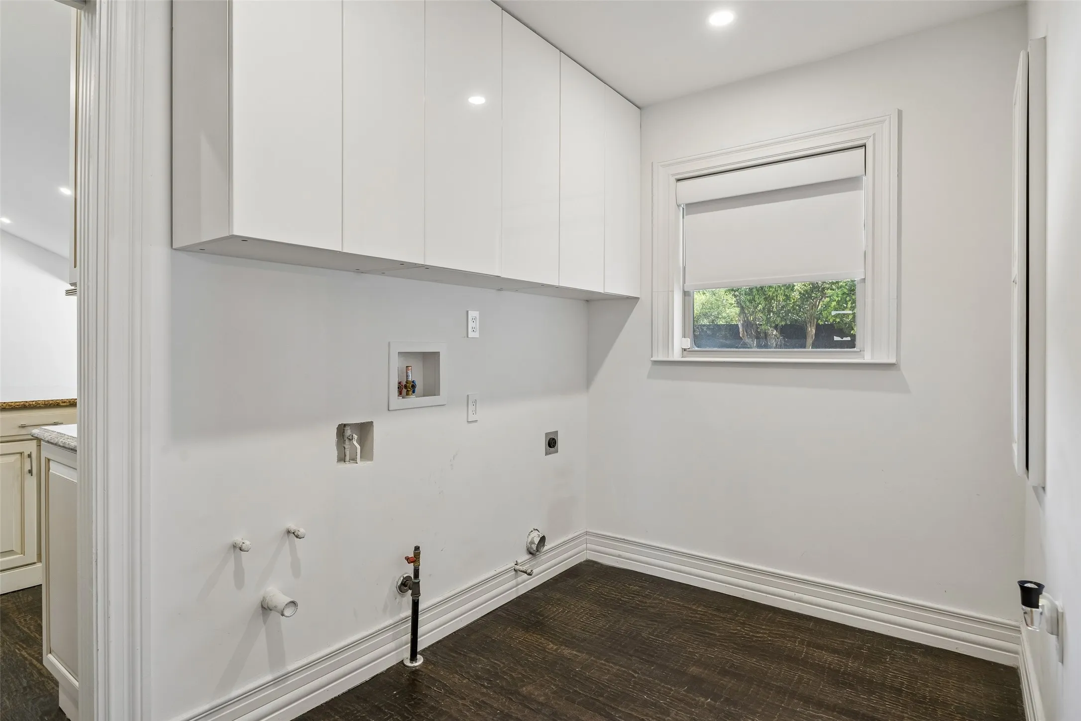 Utility room with overhead white cabinetry, dark wood-finish flooring, recessed lighting, and a window with a roller shade