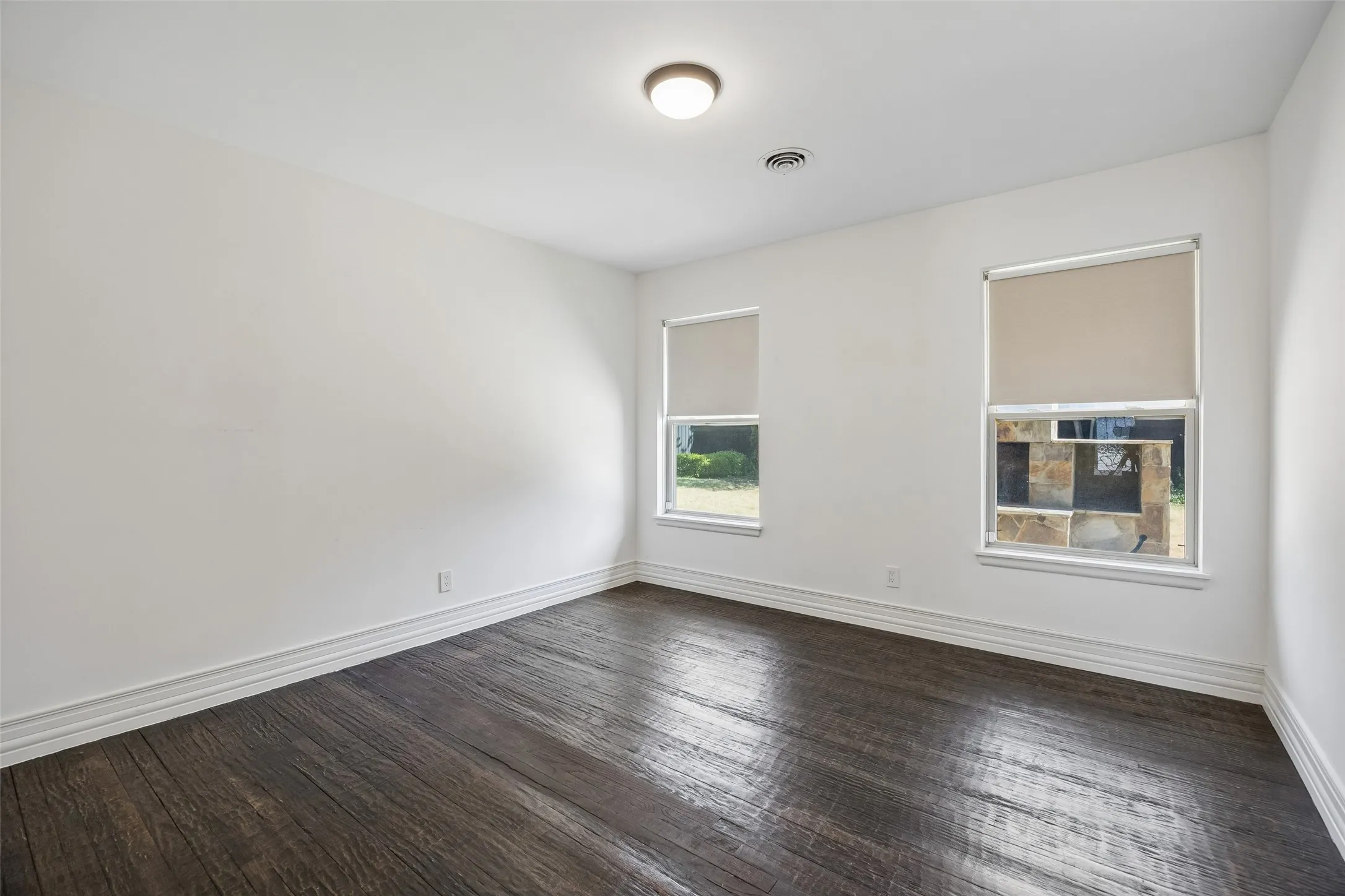 Dark wood-finish flooring, white walls, two windows with roller shades, and a ceiling-mounted light fixture