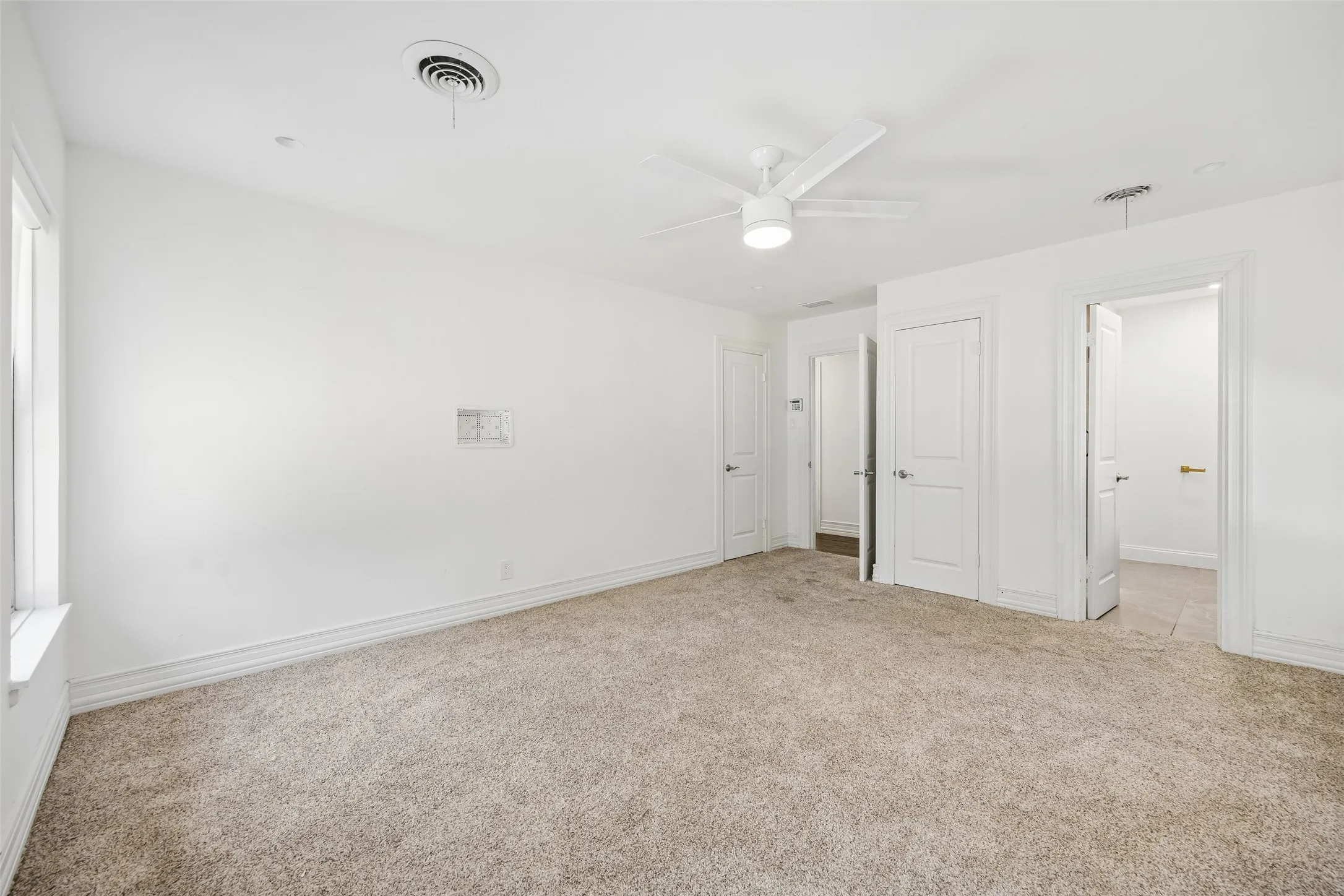 Carpeted flooring, white walls, white ceiling fan with integrated lighting, multiple white panel doors, and a window for natural light