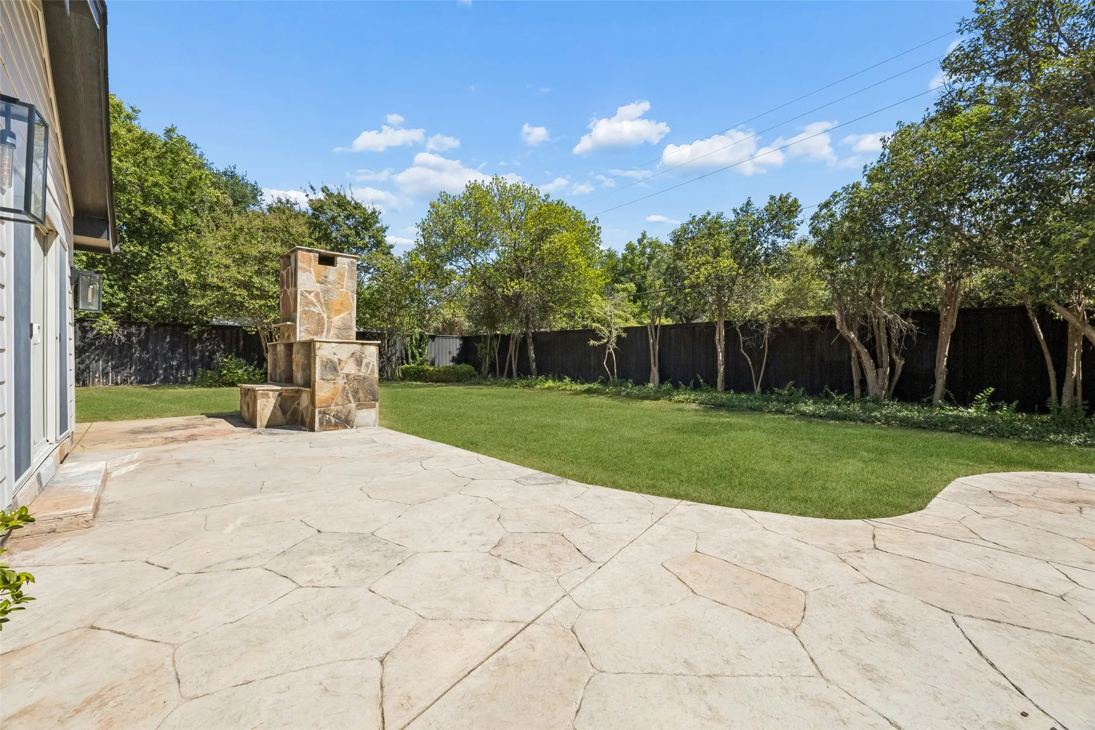 Flagstone patio with a built-in stone fireplace, expansive lawn, and perimeter fencing