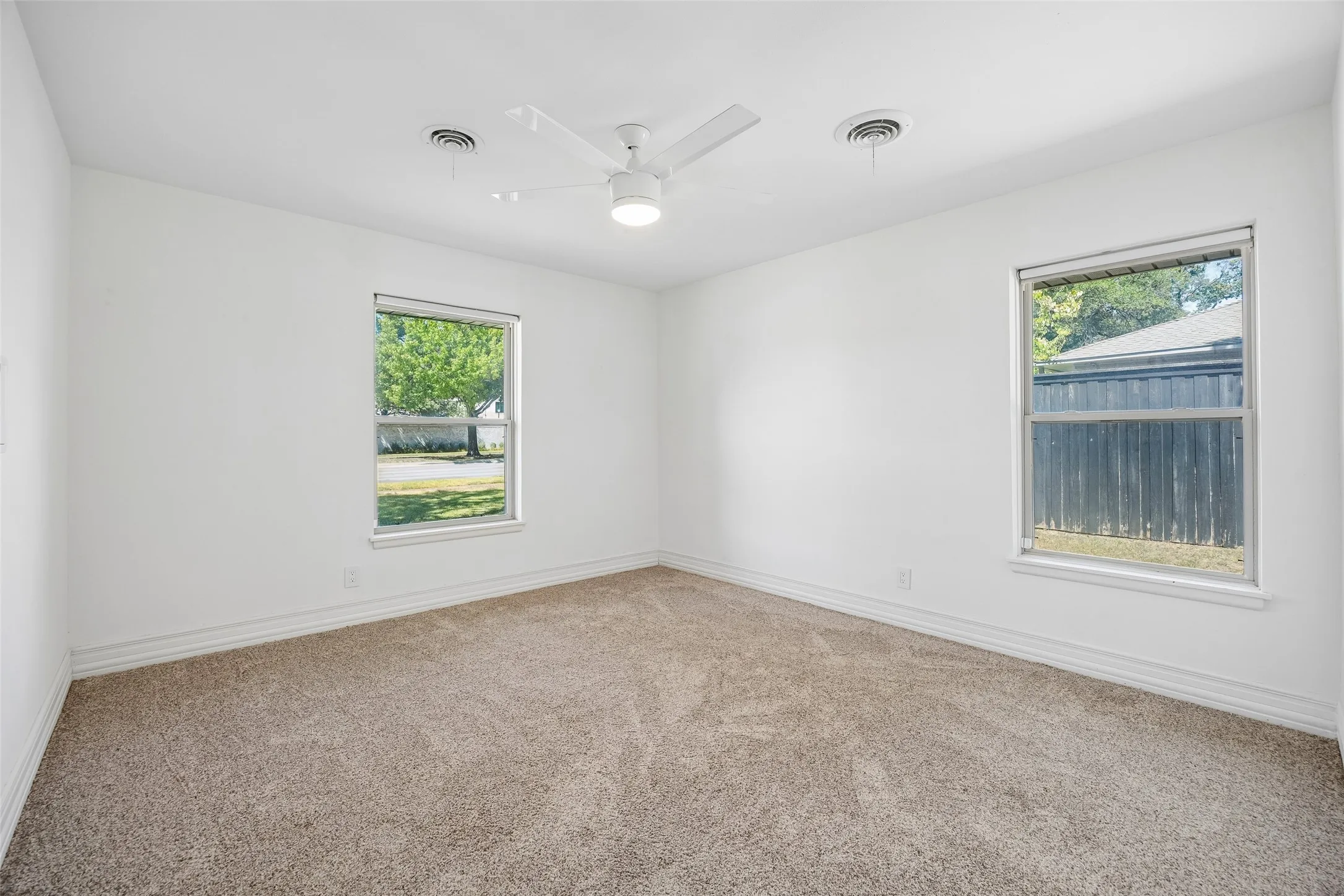 Neutral wall finishes with a ceiling fan light fixture, two windows, and carpeting