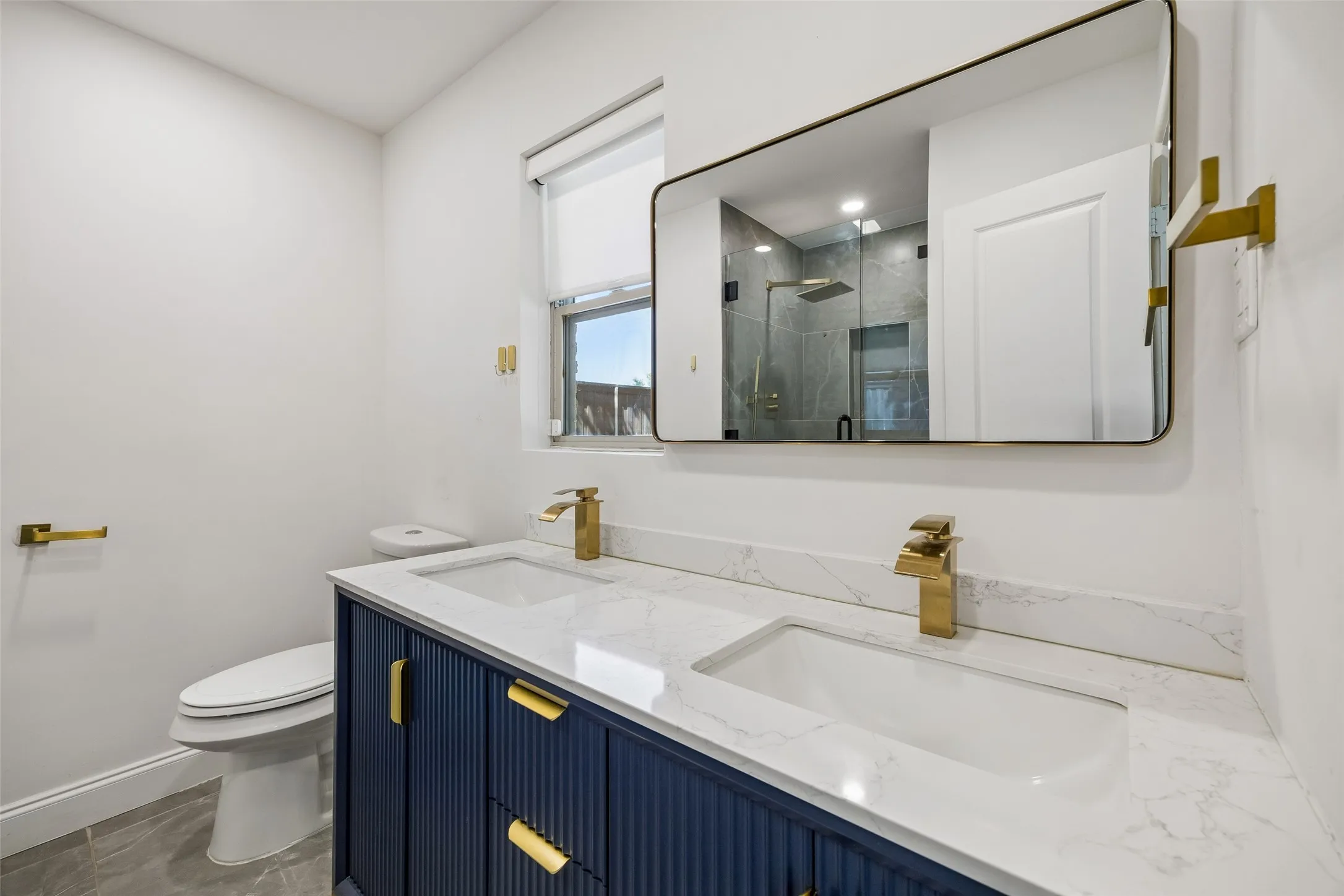 Dual sinks with brass-finish fixtures, a navy vanity with fluted detailing, and a wall-mounted mirror