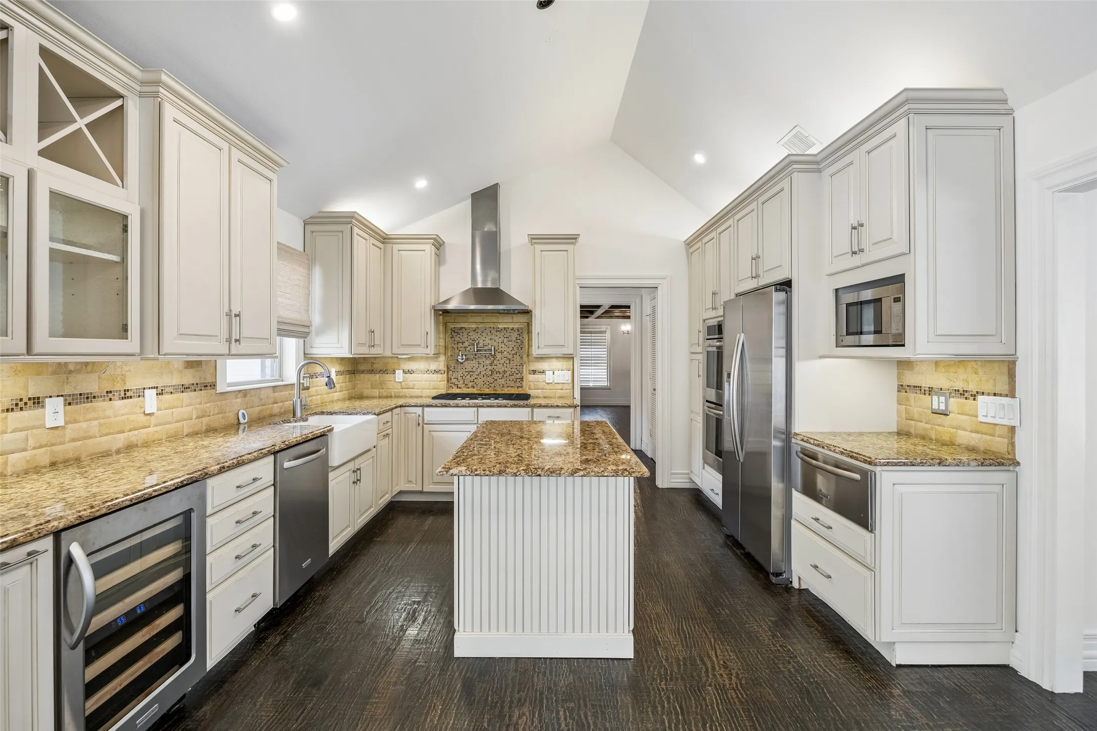 Kitchen featuring a vaulted ceiling, dark wood-finish flooring, white cabinetry, integrated stainless steel appliances, and a central island with a wood-finish countertop