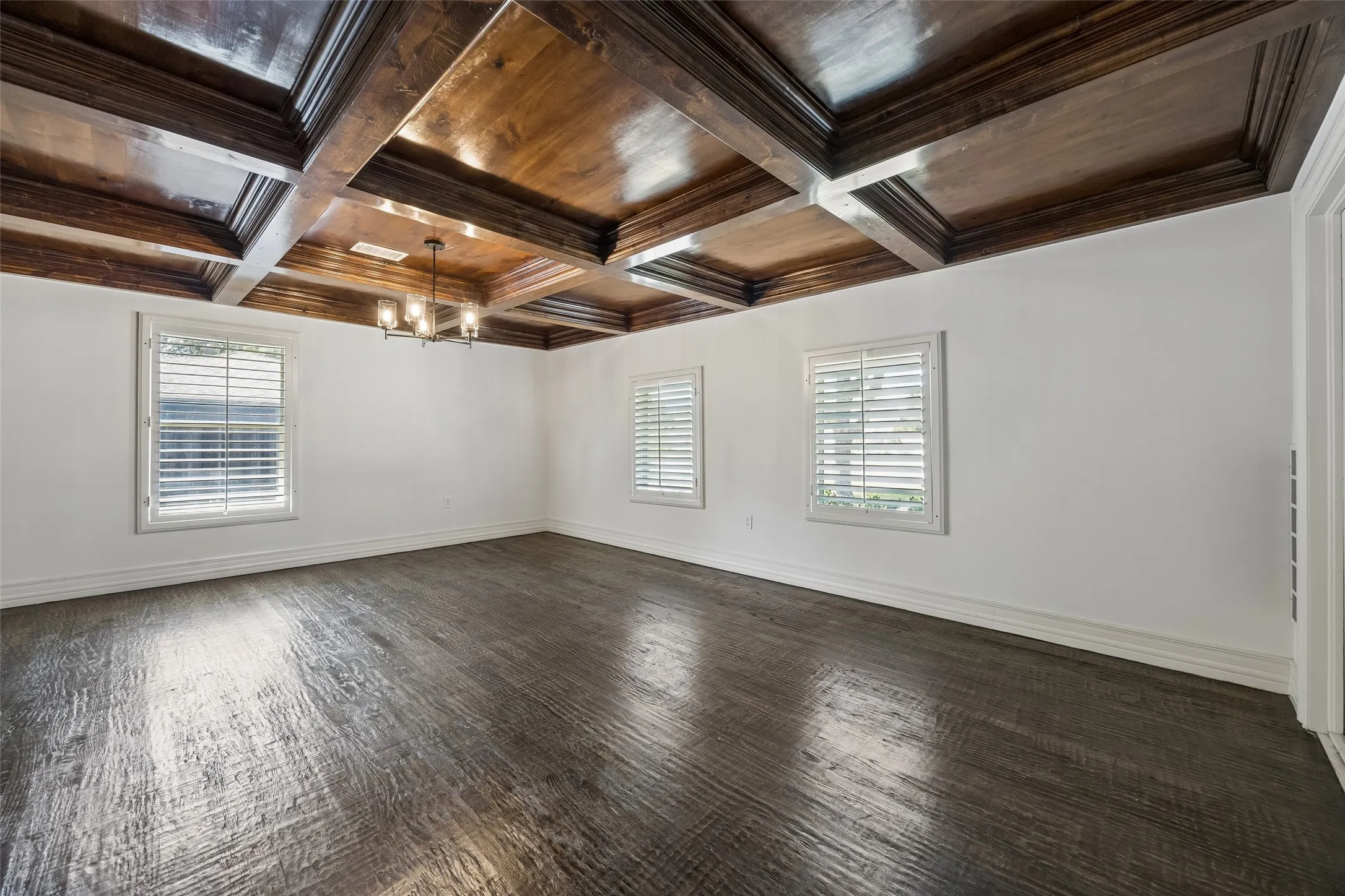 Coffered wood-finish ceiling with an attached light fixture, white walls, wood-finish flooring, and two windows with plantation shutters