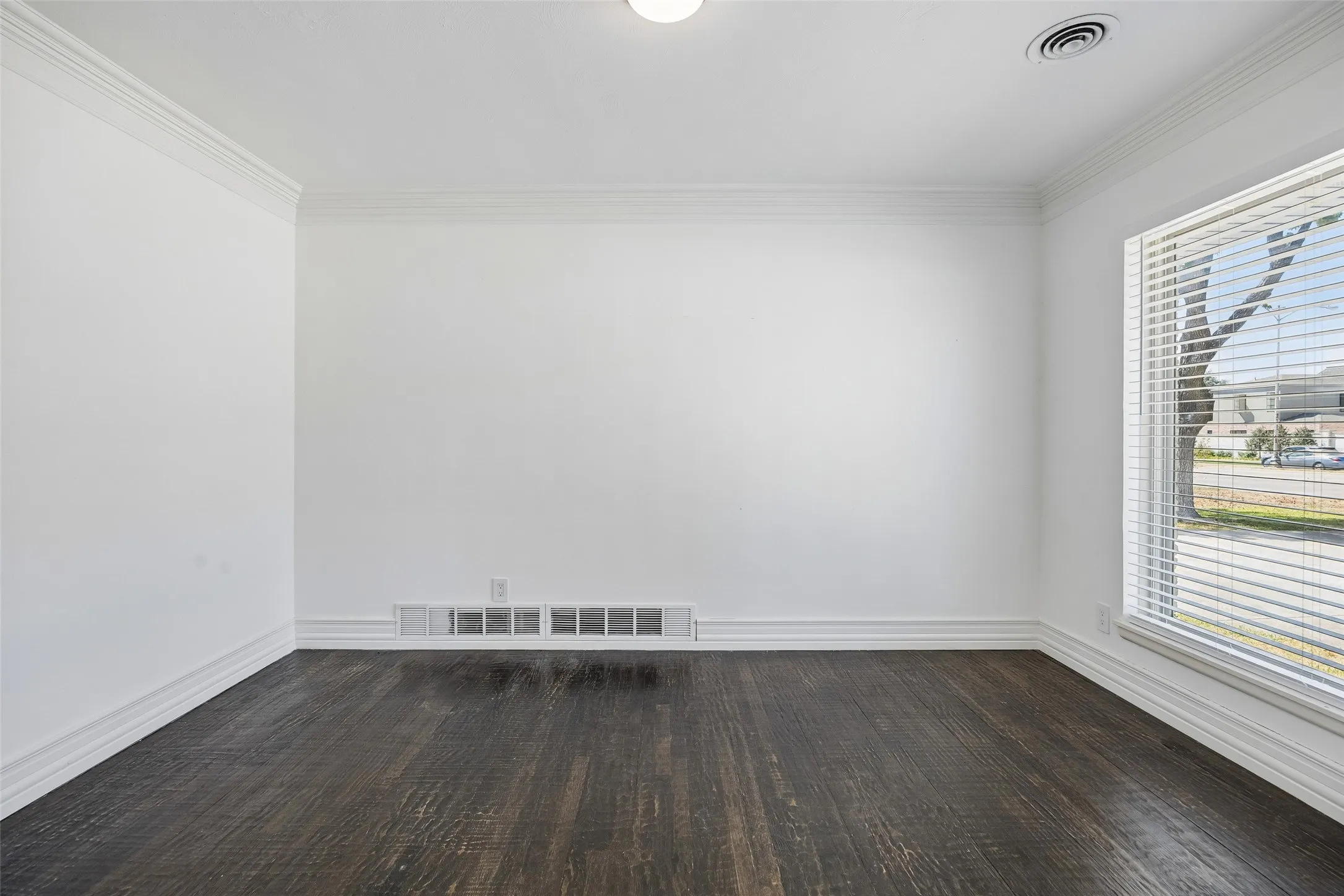 Dark wood-finish flooring with white baseboards and crown molding