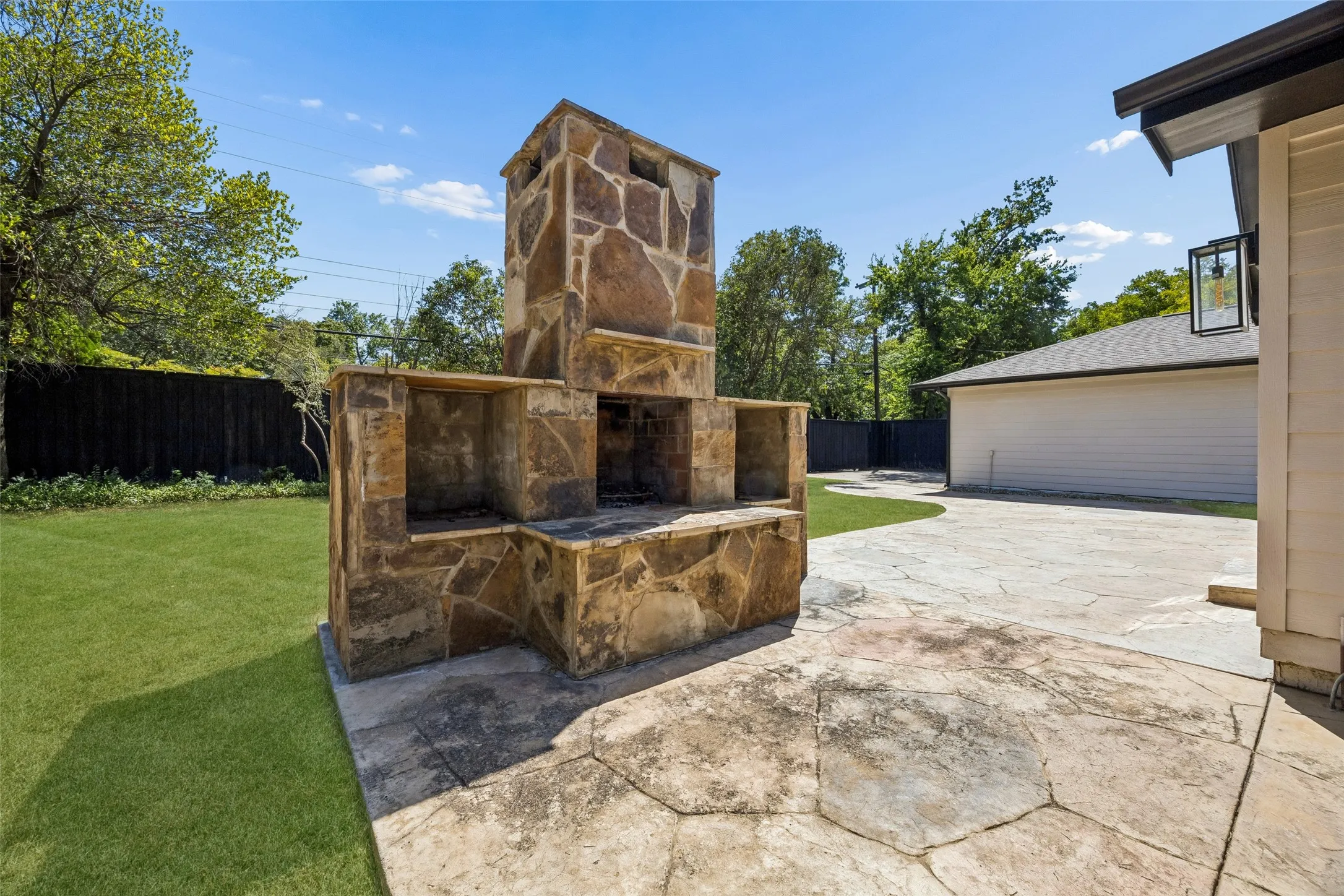 Expansive backyard featuring a stone outdoor fireplace, stamped concrete patio, manicured lawn, and privacy fencing