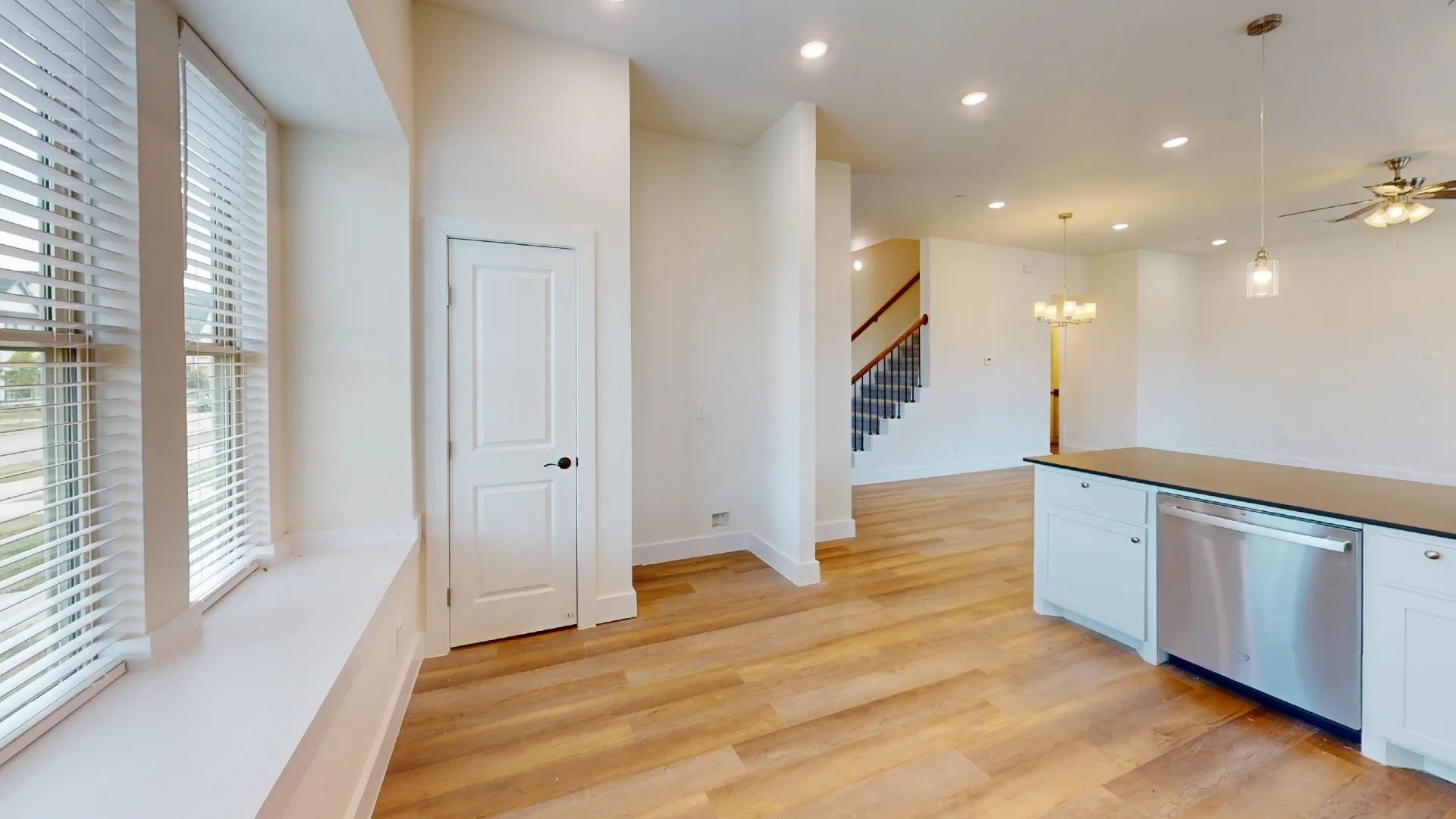 Wood-finish flooring, recessed lighting, and a stainless steel dishwasher integrated into white cabinetry with a dark countertop