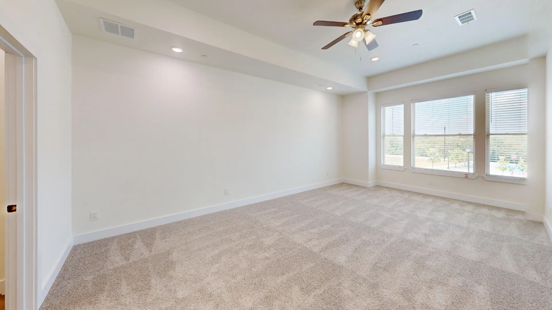 Recessed lighting, ceiling fan, three large windows with horizontal blinds, and neutral carpet flooring
