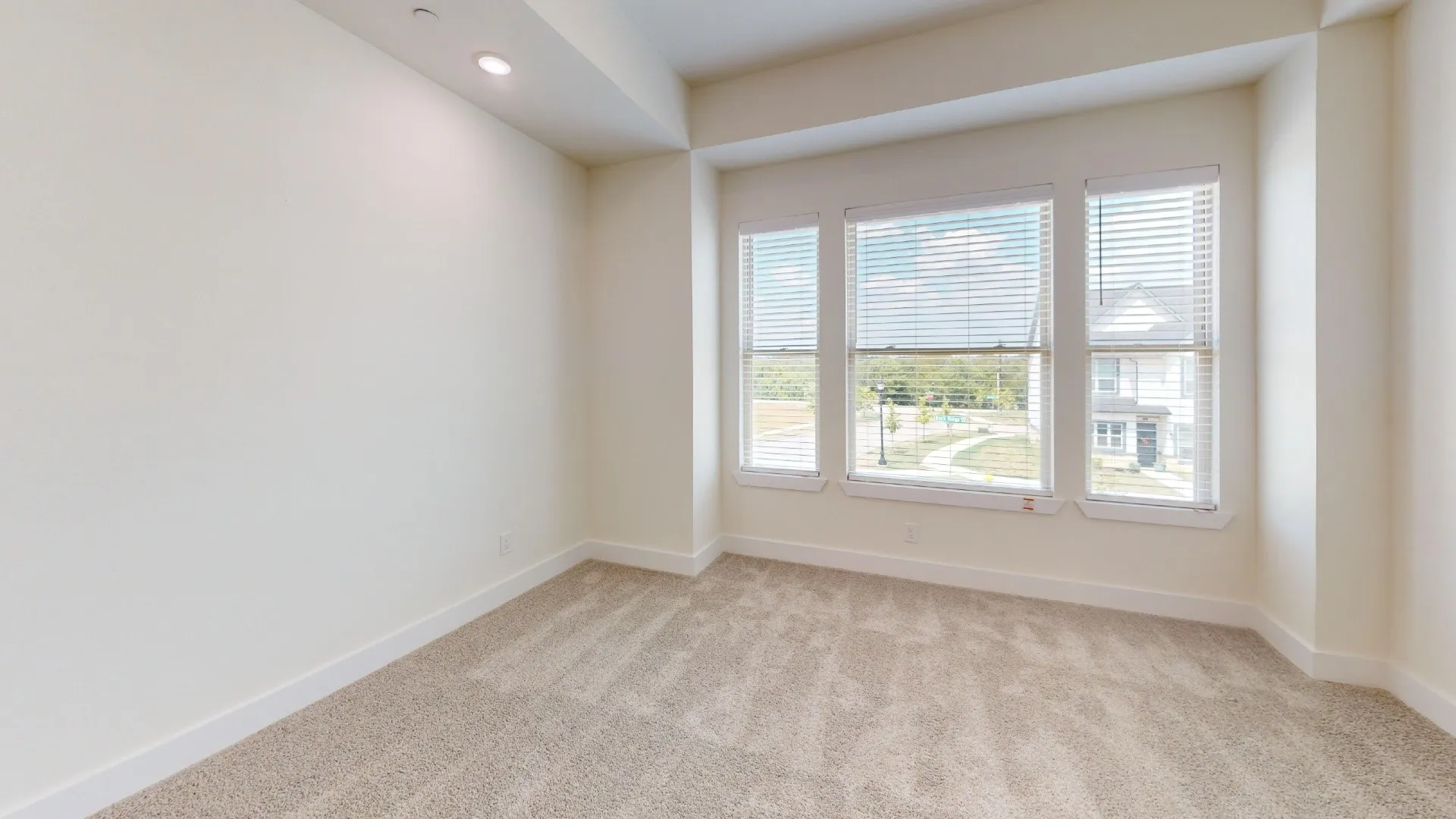 Carpeted flooring, recessed lighting, three large windows with blinds, and neutral wall tones