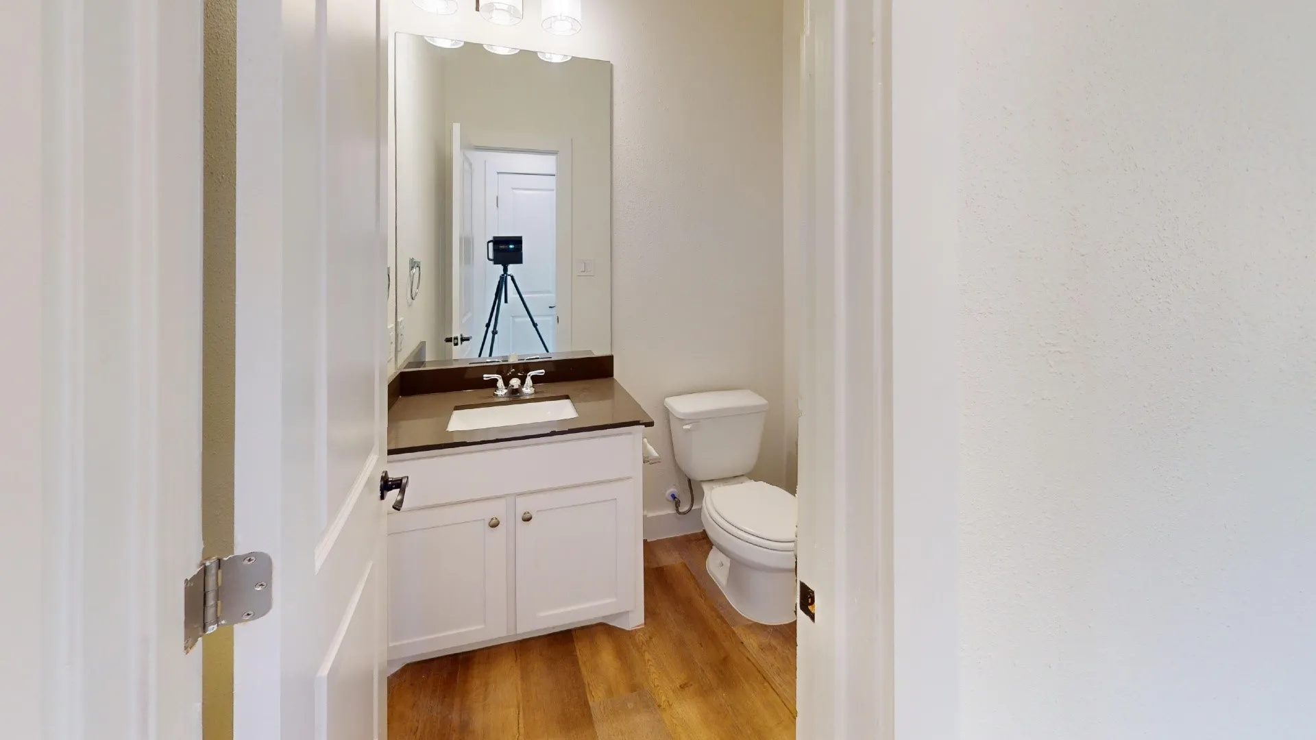 White vanity with a dark countertop, undermount sink, and wood-finish flooring
