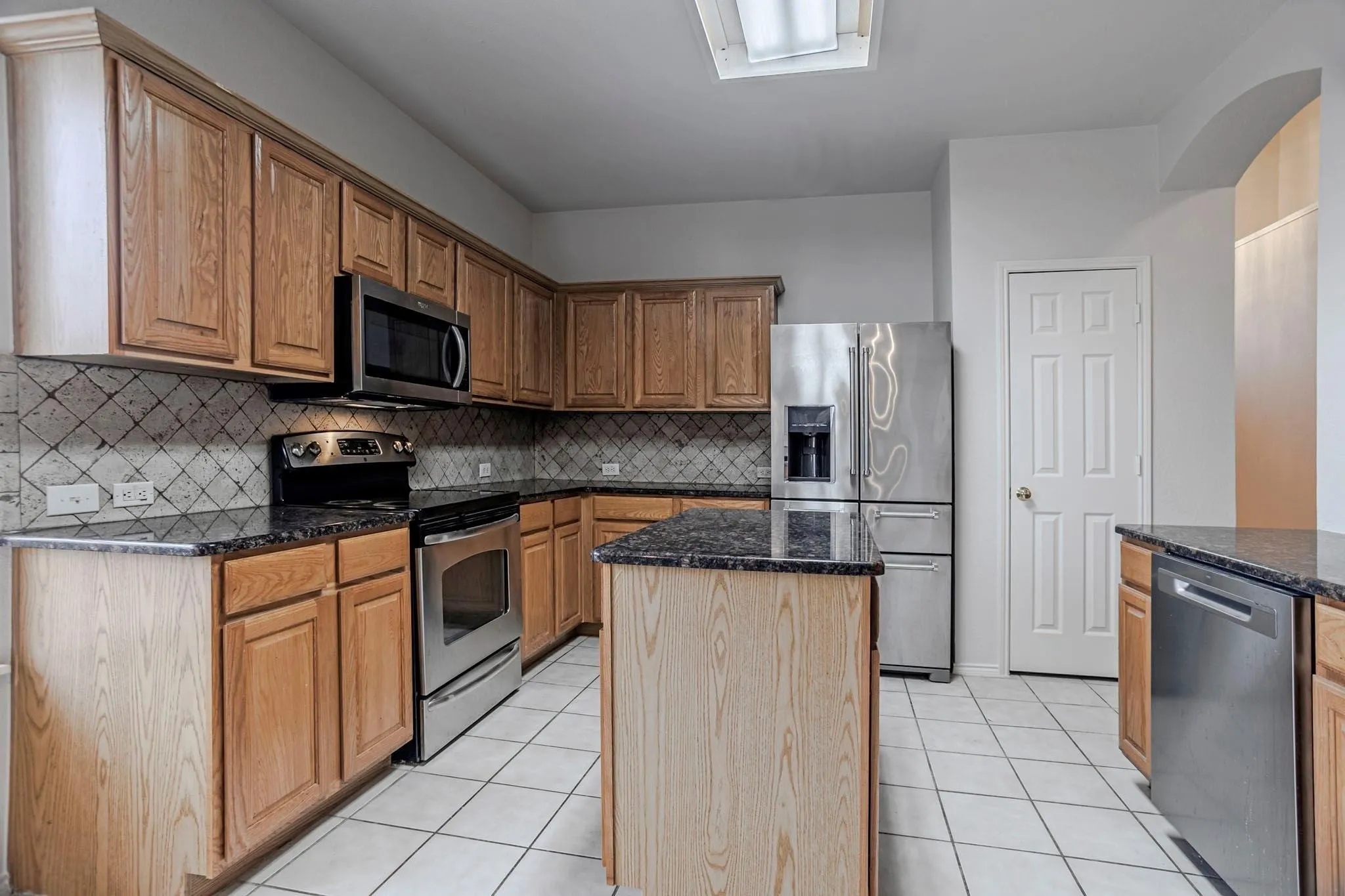 Kitchen featuring wood cabinetry, stainless steel appliances, dark stone countertops, a central island, and tile flooring