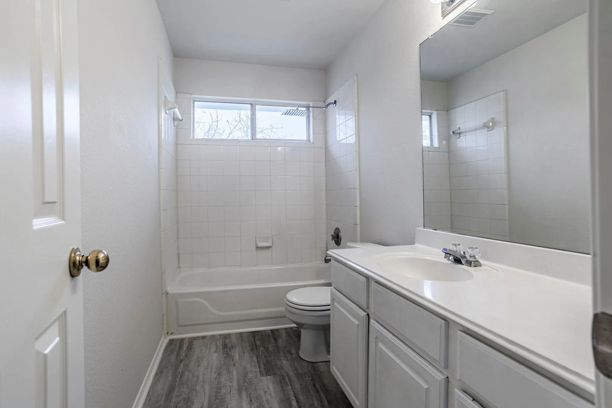 Bathroom featuring a shower/tub combination, white subway tile surround, wood-finish flooring, and a vanity with an integrated sink