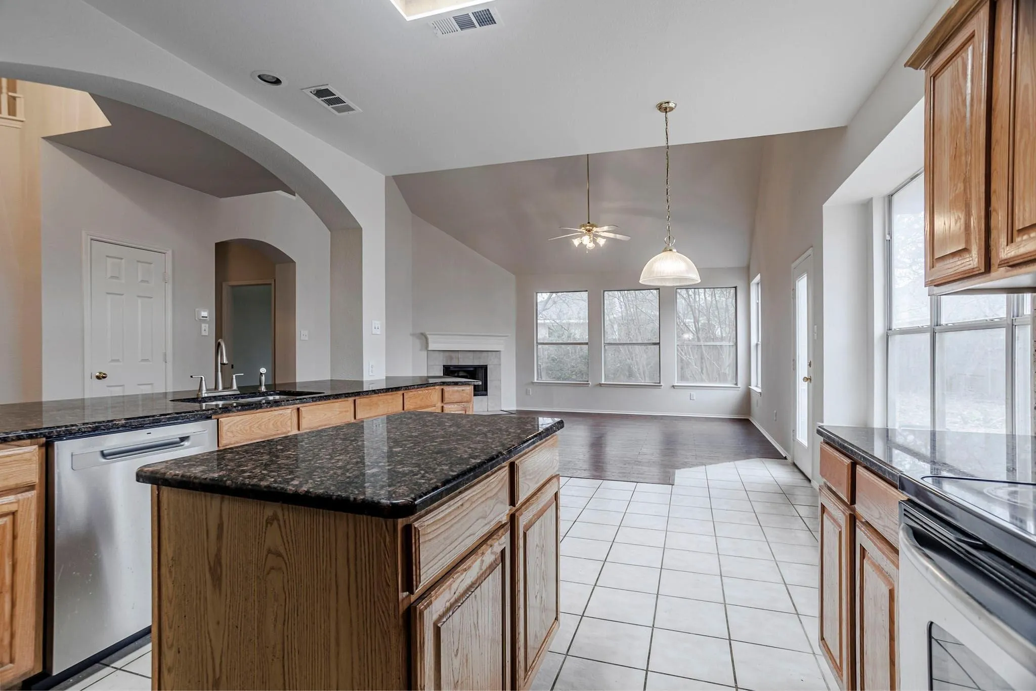 Kitchen featuring wood cabinetry, dark stone countertops, stainless steel dishwasher, and tile flooring