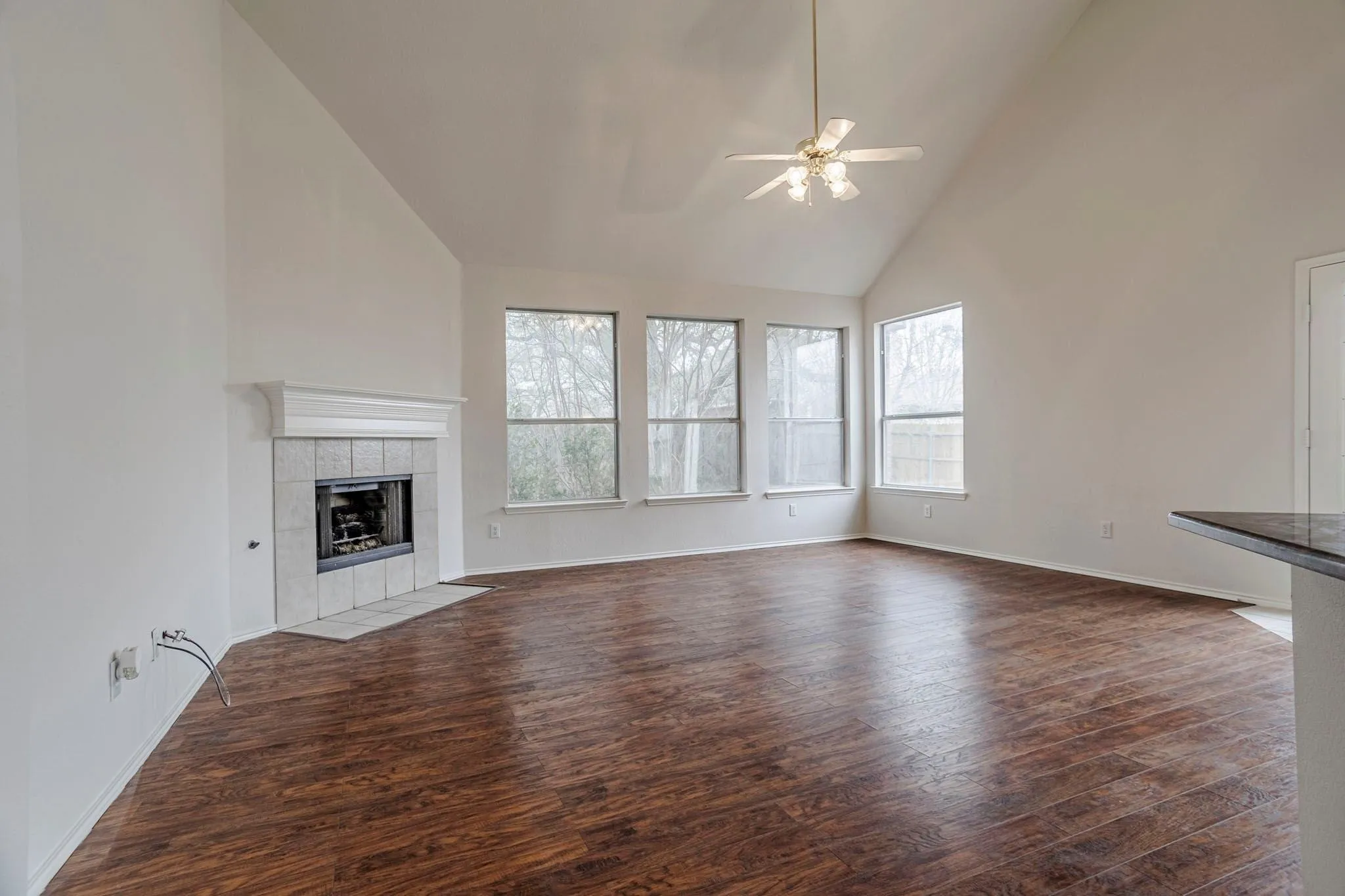 Vaulted ceiling, wood-finish flooring, tiled fireplace, multiple windows, and a ceiling fan