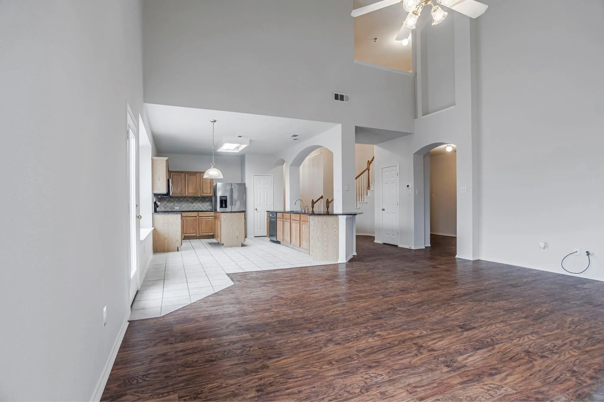 Open-concept living area with wood-finish flooring, high ceilings, and a ceiling fan