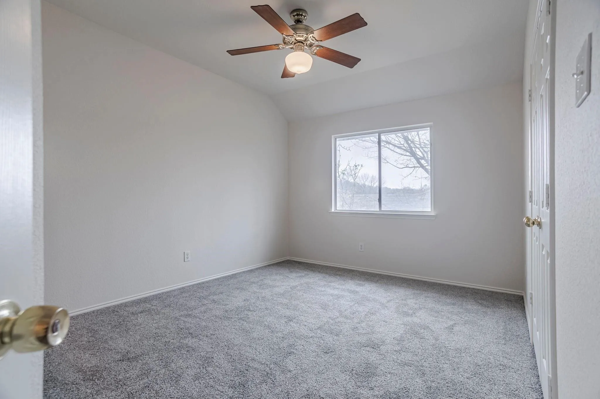 Sloped ceiling with an integrated ceiling fan, carpet flooring, and a large window