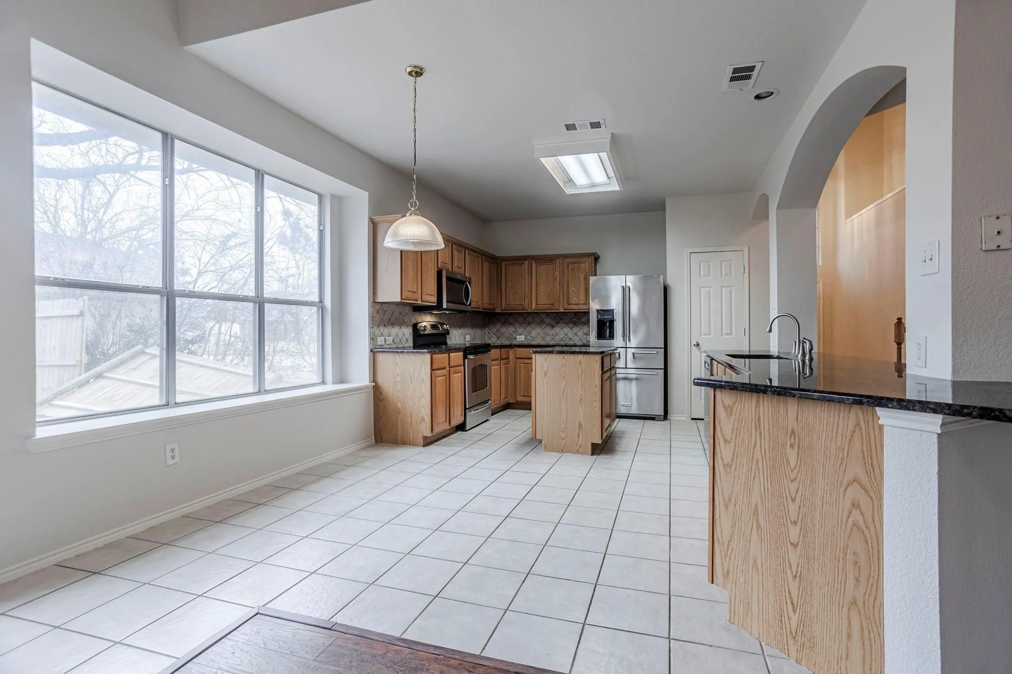 Kitchen featuring a large multi-pane window, tile flooring, wood cabinetry, stone countertops, and an arched entryway