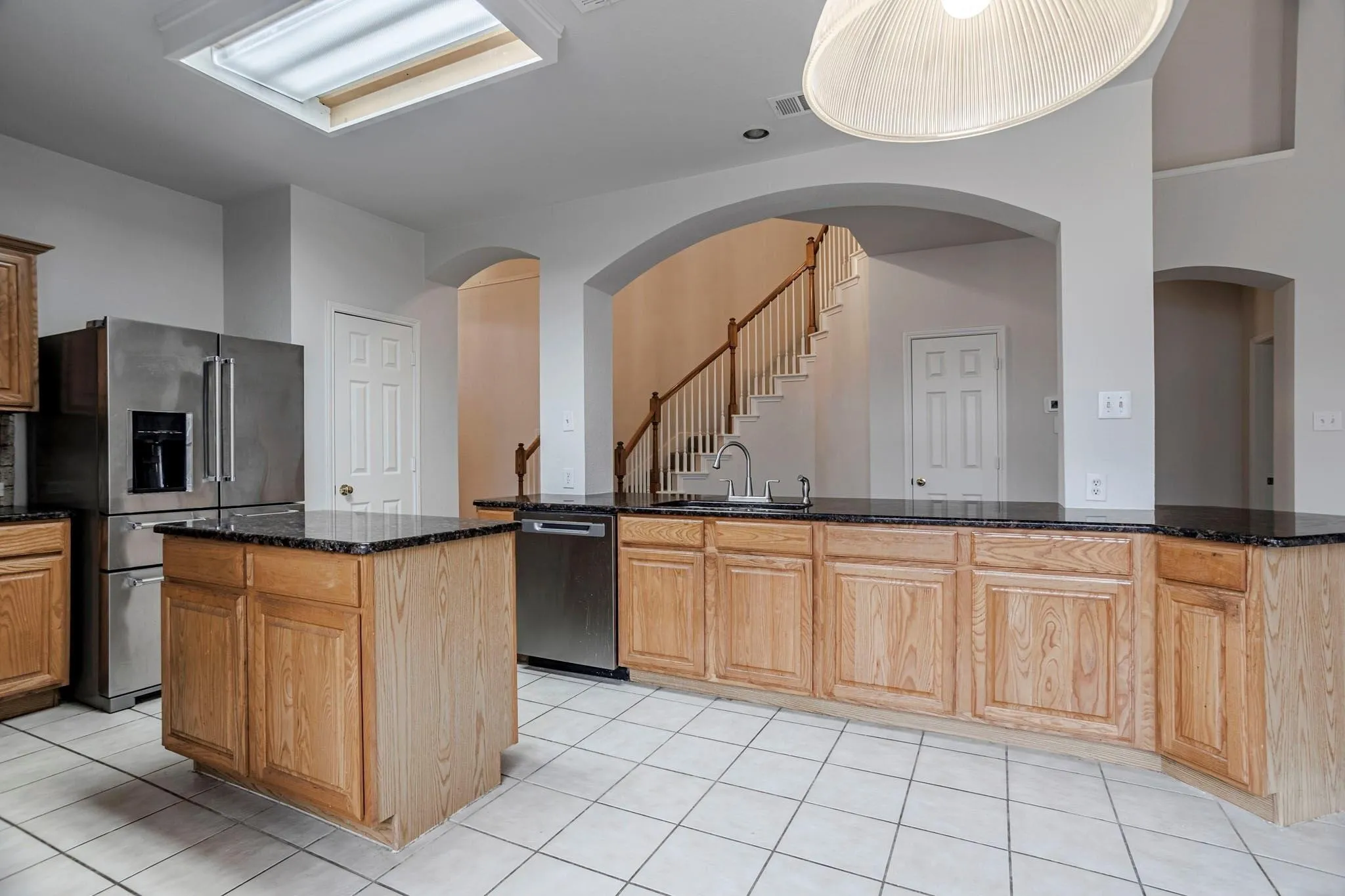 Kitchen featuring wood cabinetry, dark countertops, a central island, stainless steel appliances, and a skylight