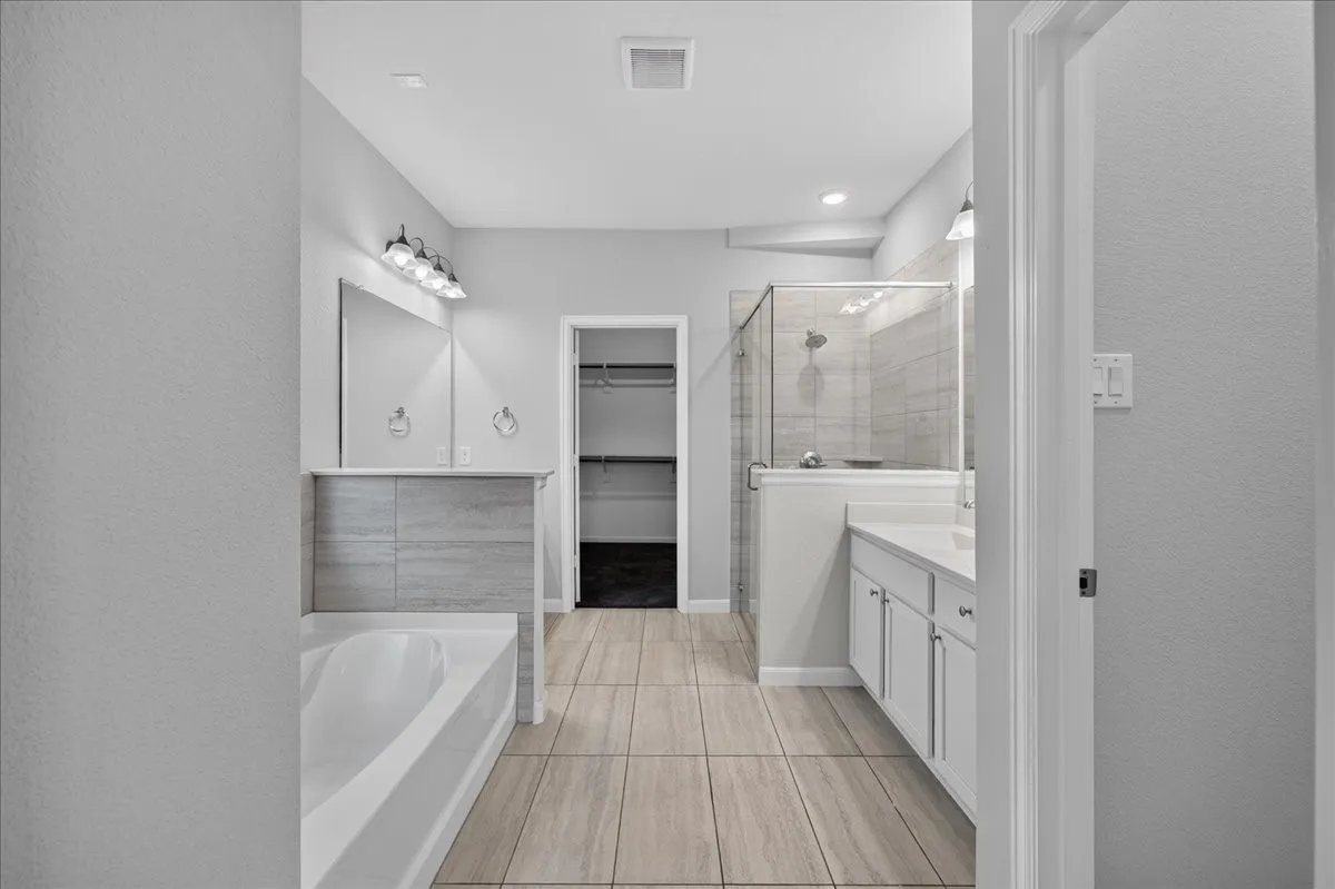 Tiled flooring, built-in bathtub, glass-enclosed shower, dual vanity with white cabinetry, and recessed lighting