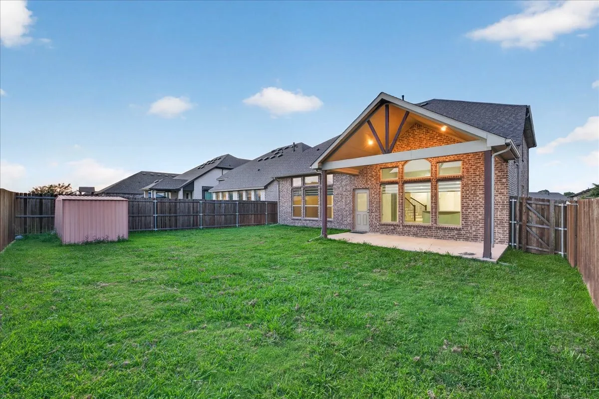 Expansive fenced backyard featuring a covered patio, brick exterior, and a storage shed