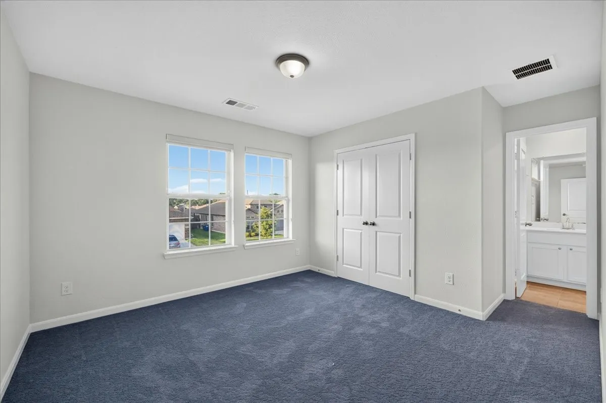 Double windows with grid panes, textured blue carpeting, bi-fold closet doors with black hardware, and a ceiling-mounted light fixture