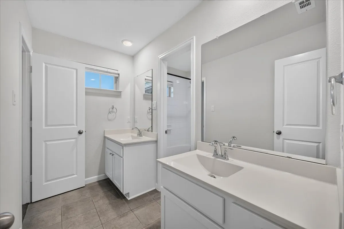 Dual vanity with integrated sinks and white cabinetry, a large wall-mounted mirror, and tile flooring