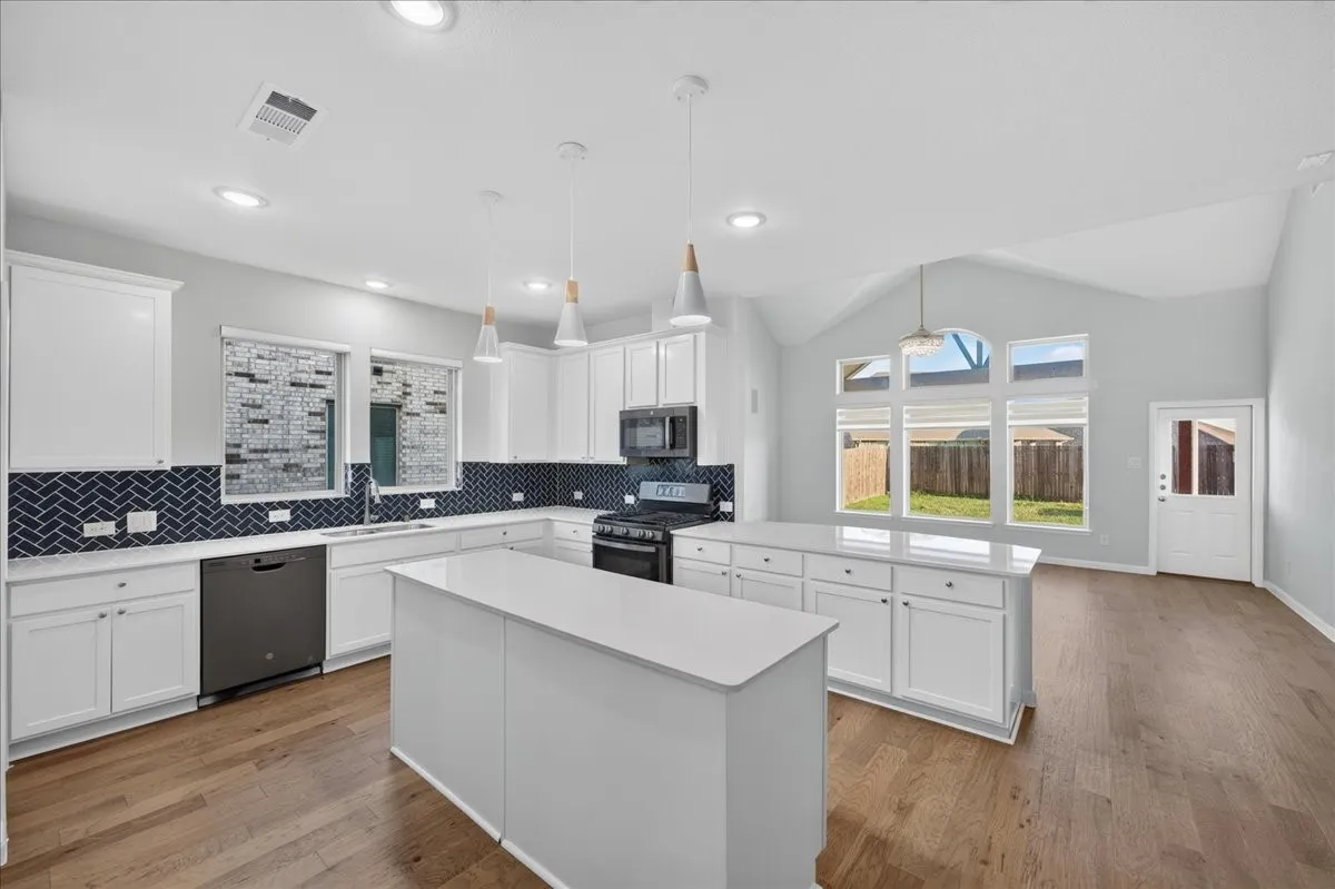 Kitchen featuring dual islands, white shaker-style cabinetry, dark herringbone tile backsplash, and stainless steel appliances