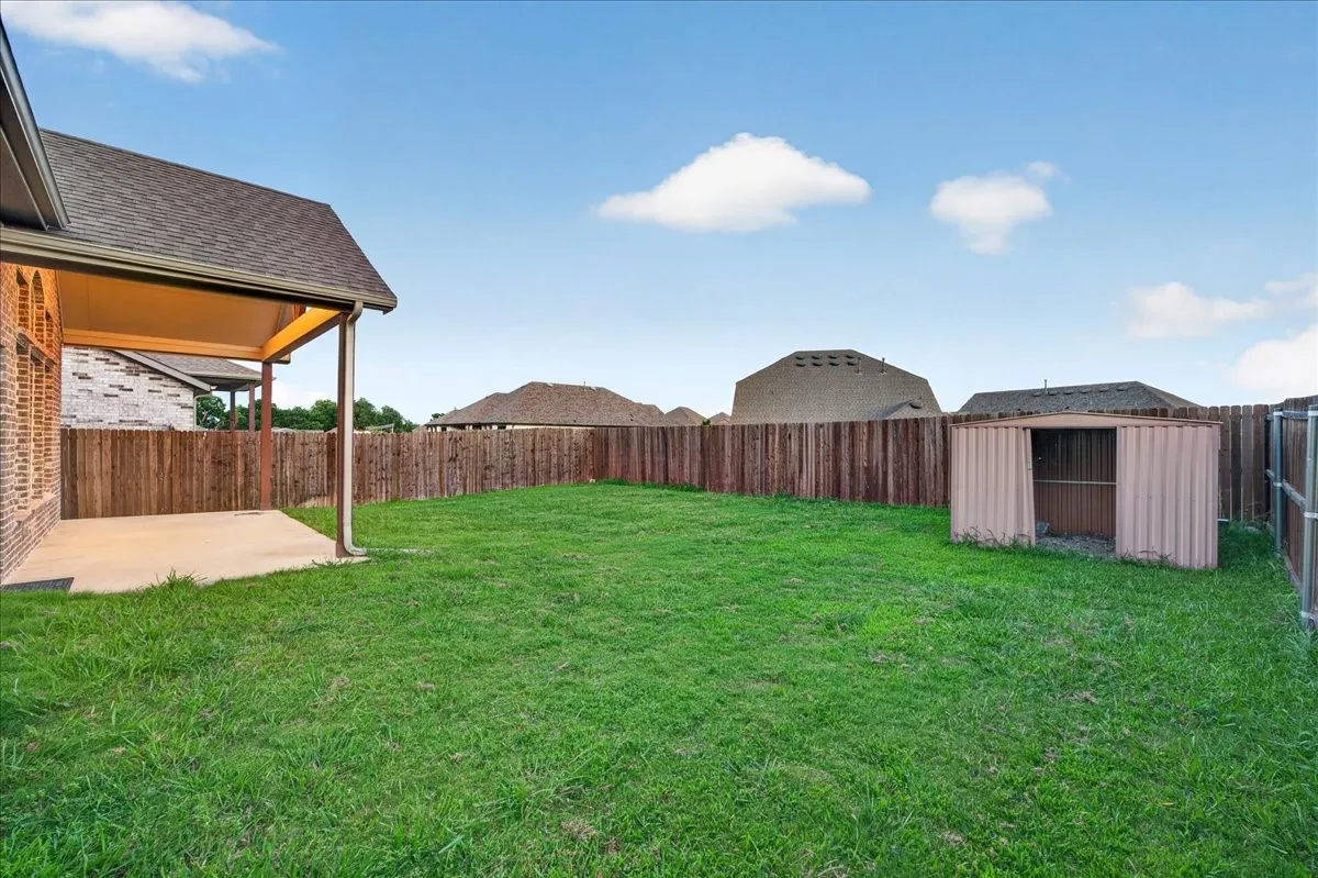 Expansive green lawn with a covered patio, wood privacy fence, and a storage shed