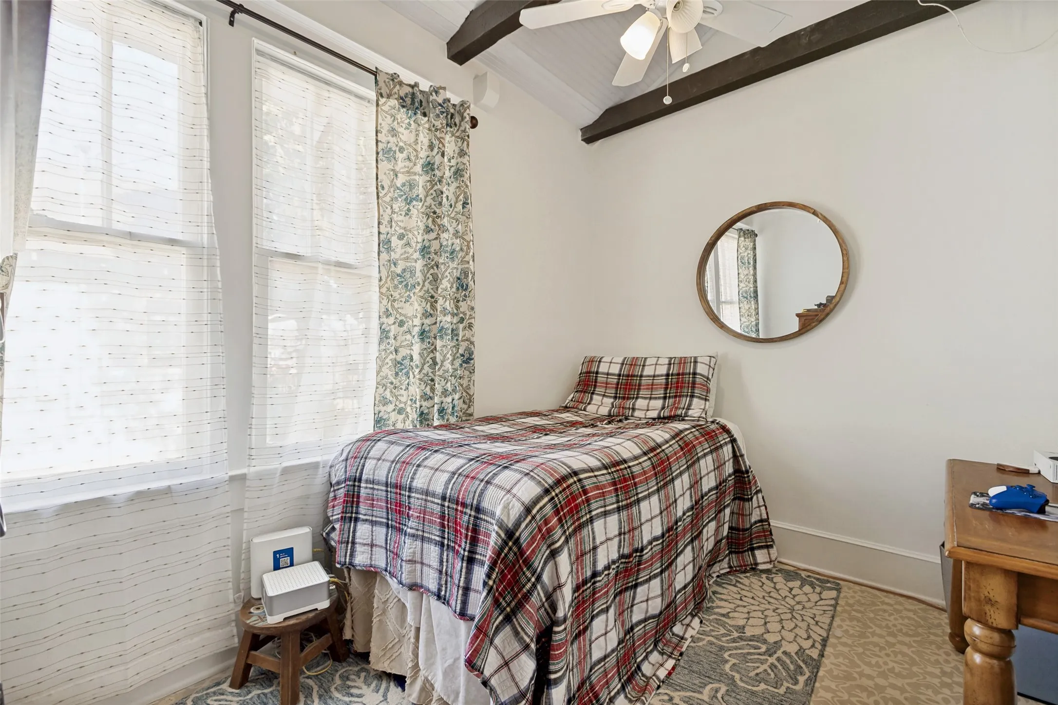Vaulted ceiling with exposed wood beams, dual windows, and a ceiling fan