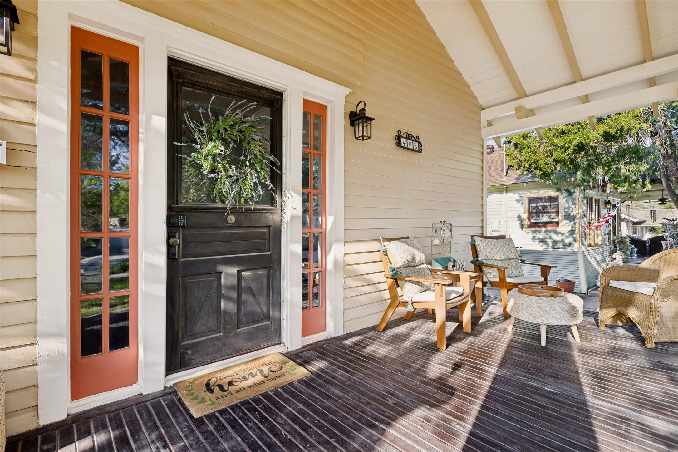 Covered porch with wood-finish flooring, light-colored siding, and a dark entry door flanked by sidelights