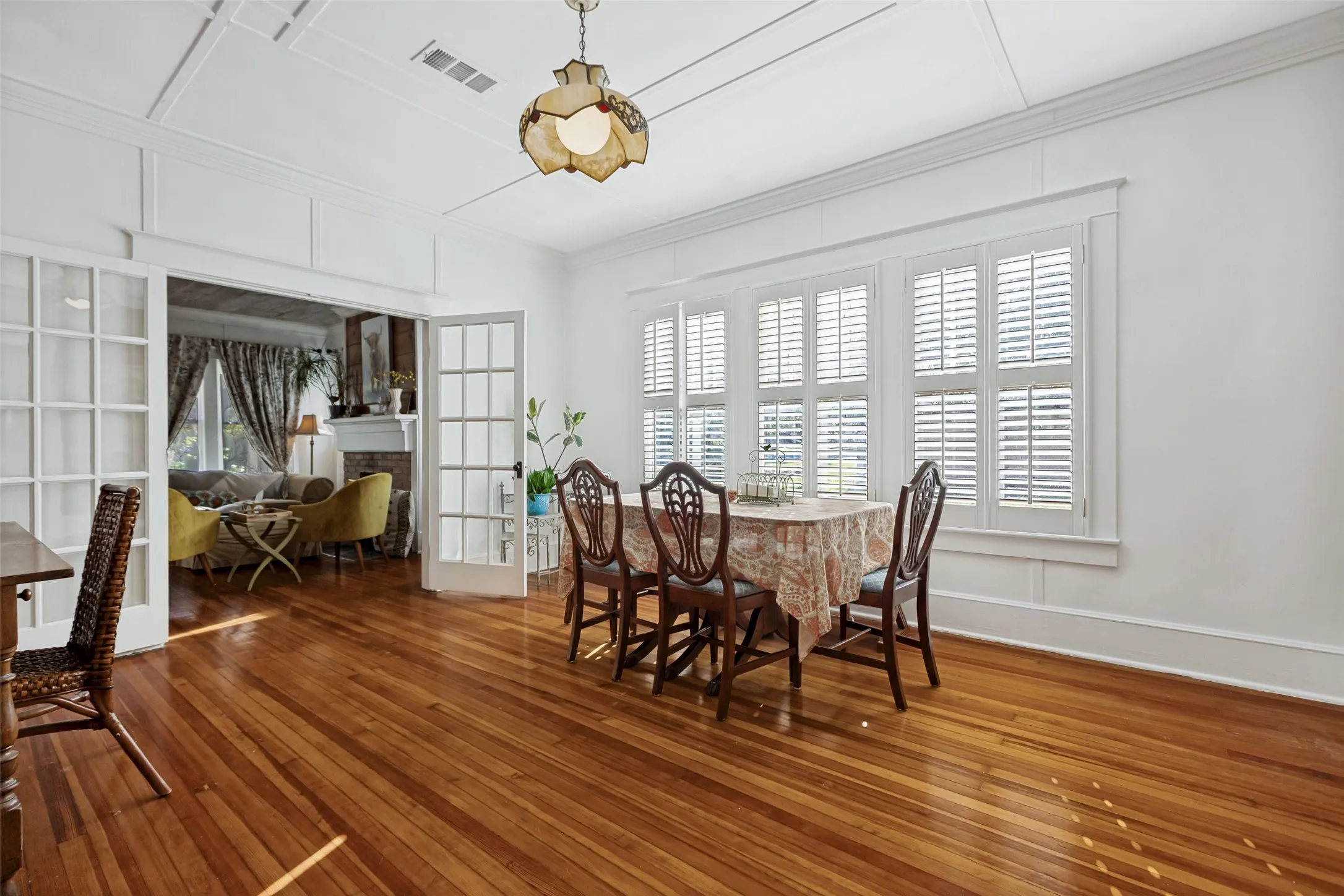 Hardwood flooring throughout, multiple windows with plantation shutters, coffered ceiling, and white French doors